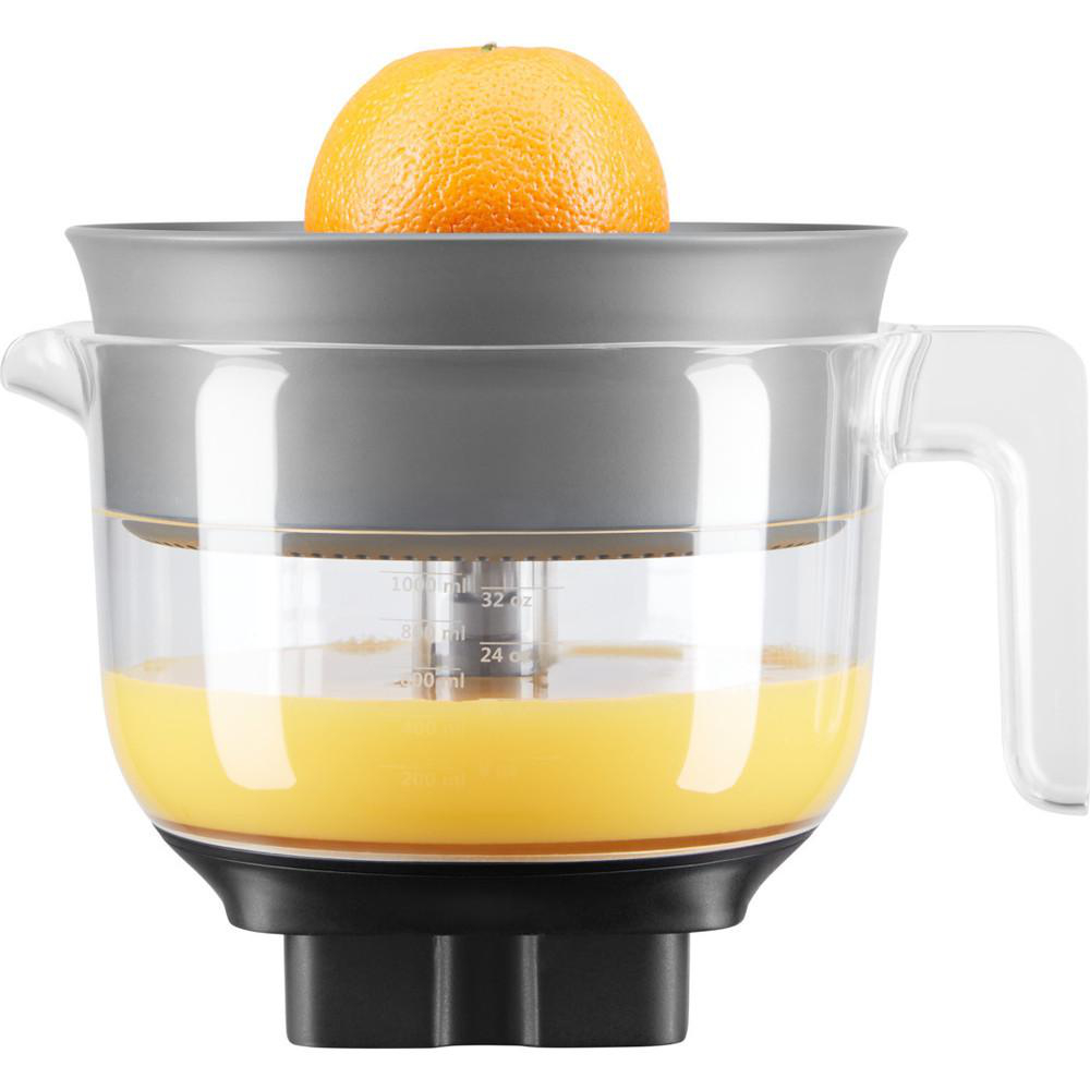 Ein Entsafter mit einer halbierten Orange oben und Saft im Inneren. Es ist weiß mit einem grauen Oberteil und einem schwarzen Sockel.
