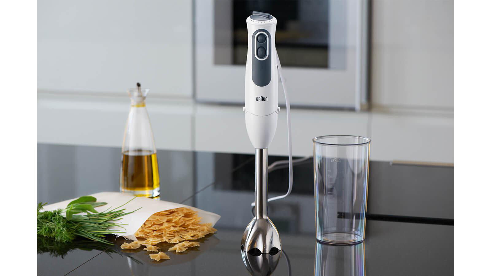 Weißer und grauer Handmixer mit Zubehör auf schwarzer Oberfläche. Hintergrund ist eine Küche.