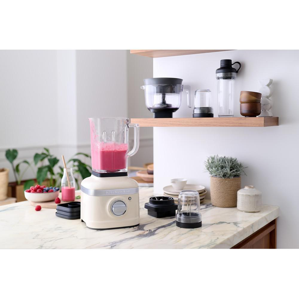 Eine Küche mit einem Mixer, der einen rosa Smoothie zubereitet. Weitere Artikel auf Theke/Regal: Gläser, eine Schüssel und andere Mixer-Teile.