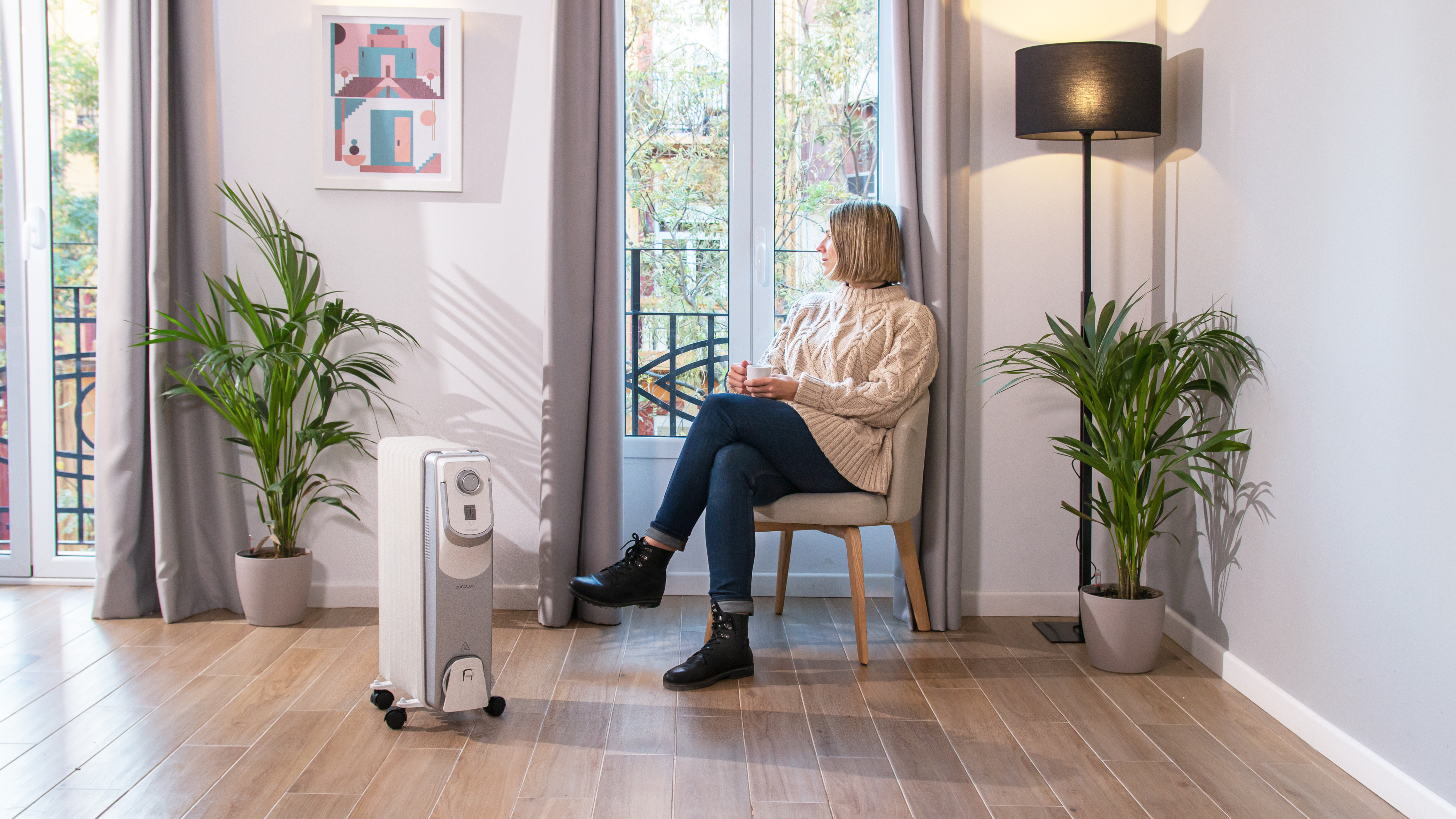 Una mujer sentada en una habitación con un calefactor y plantas, mirando por una ventana.