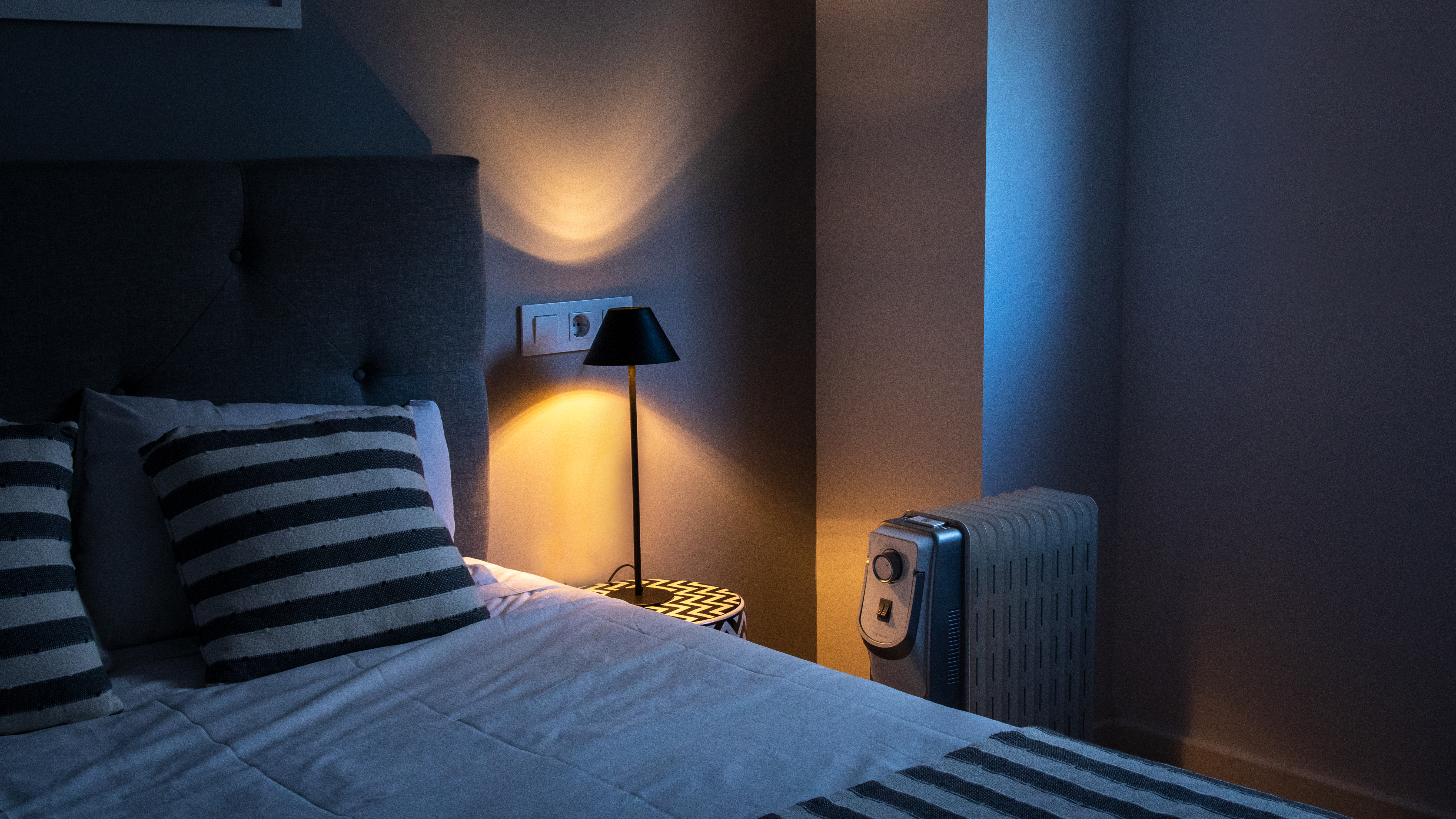 Esquina del dormitorio con cama, lámpara y calefactor.
