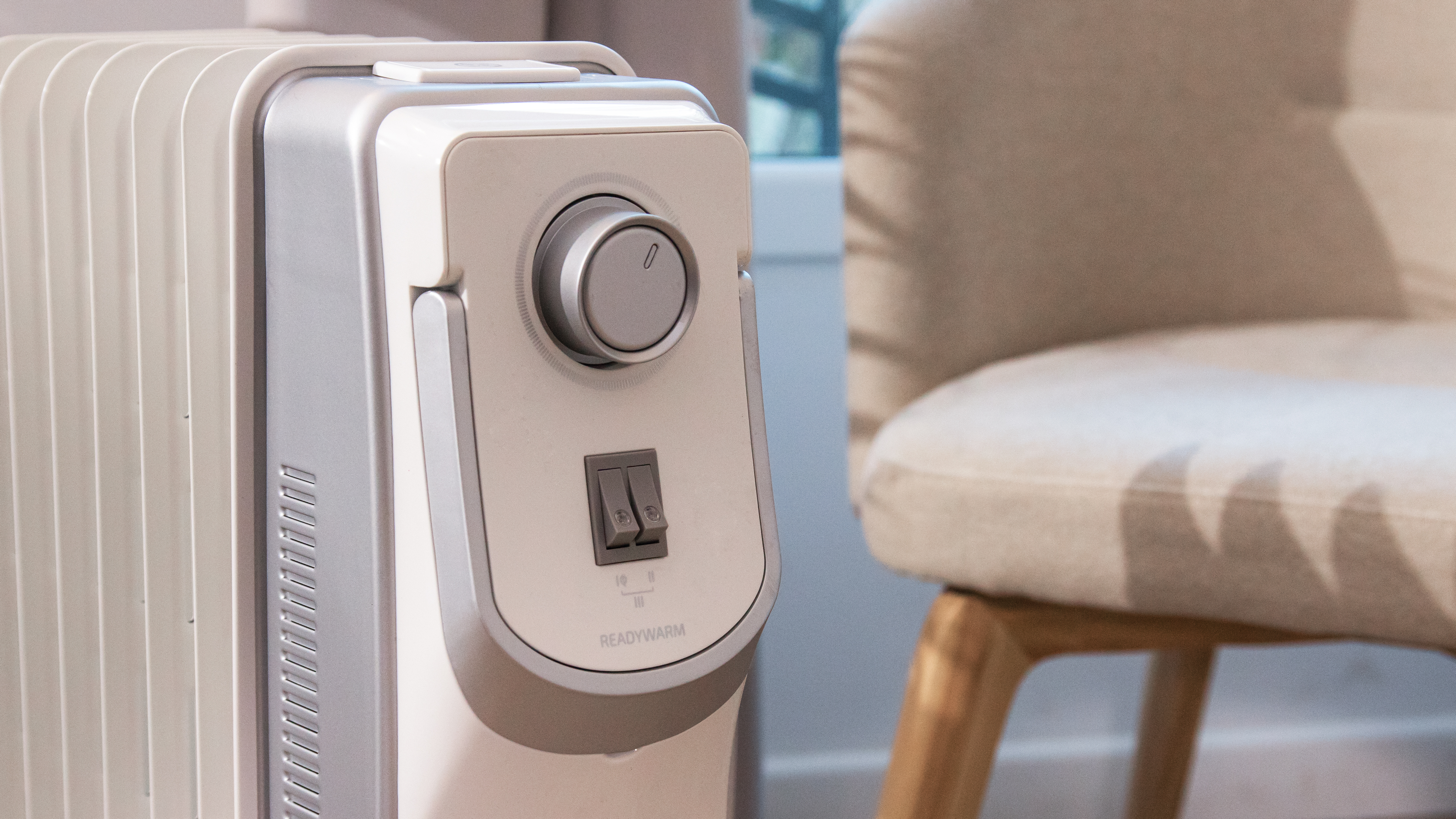 Un calefactor de aceite con una perilla de control y un interruptor junto a una silla.