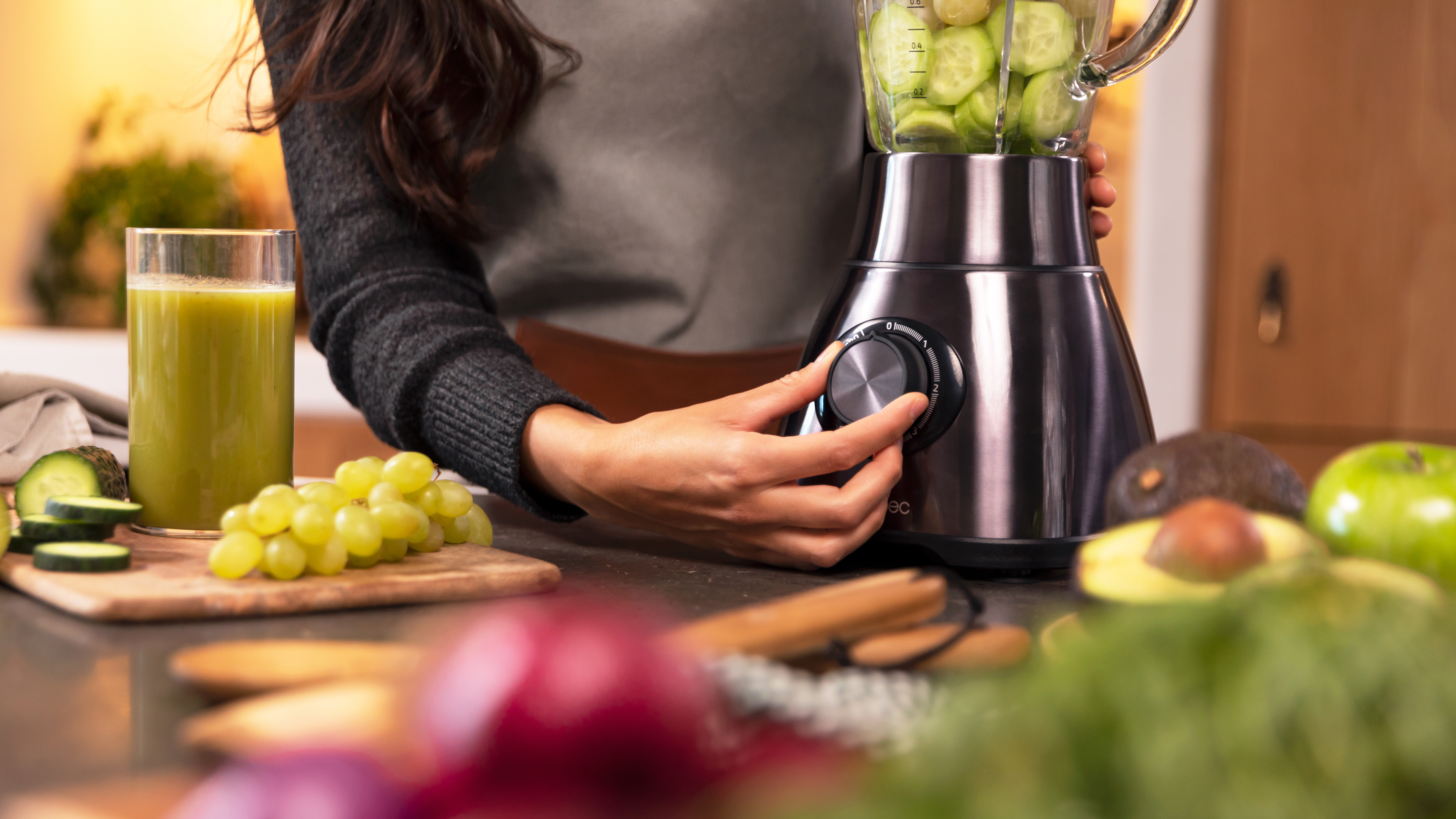 Manos de una persona ajustando una licuadora con frutas y verduras en una encimera.