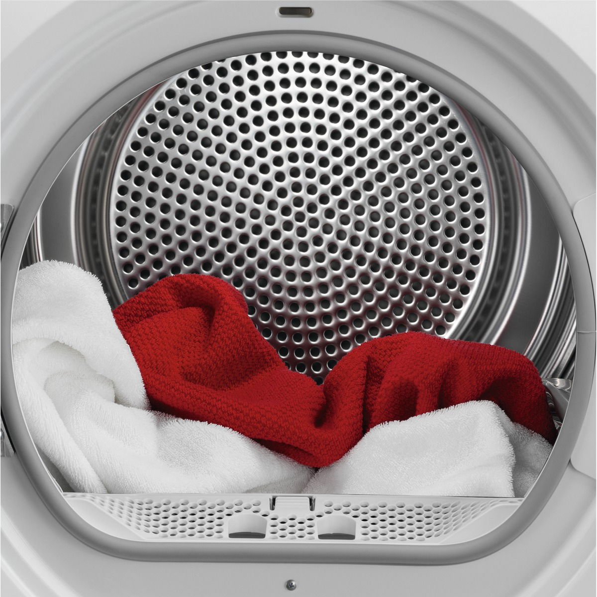 Dentro de una secadora con ropa blanca y roja, una malla metálica y un marco blanco.