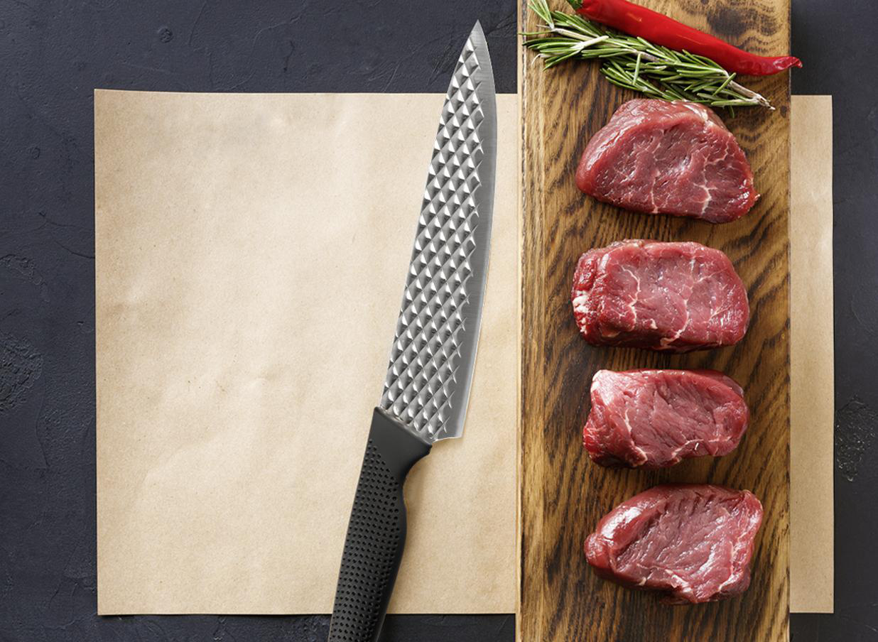 Ein Kochmesser, rohe Rindersteaks, Rosmarin und eine rote Paprika liegen auf einem Holzbrett und leerem Papier.