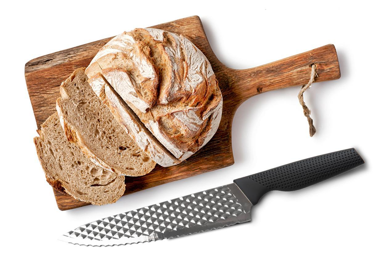 Ein Brot, geschnitten und ganz, auf einem Holzbrett. Ein gezahntes Messer liegt daneben.