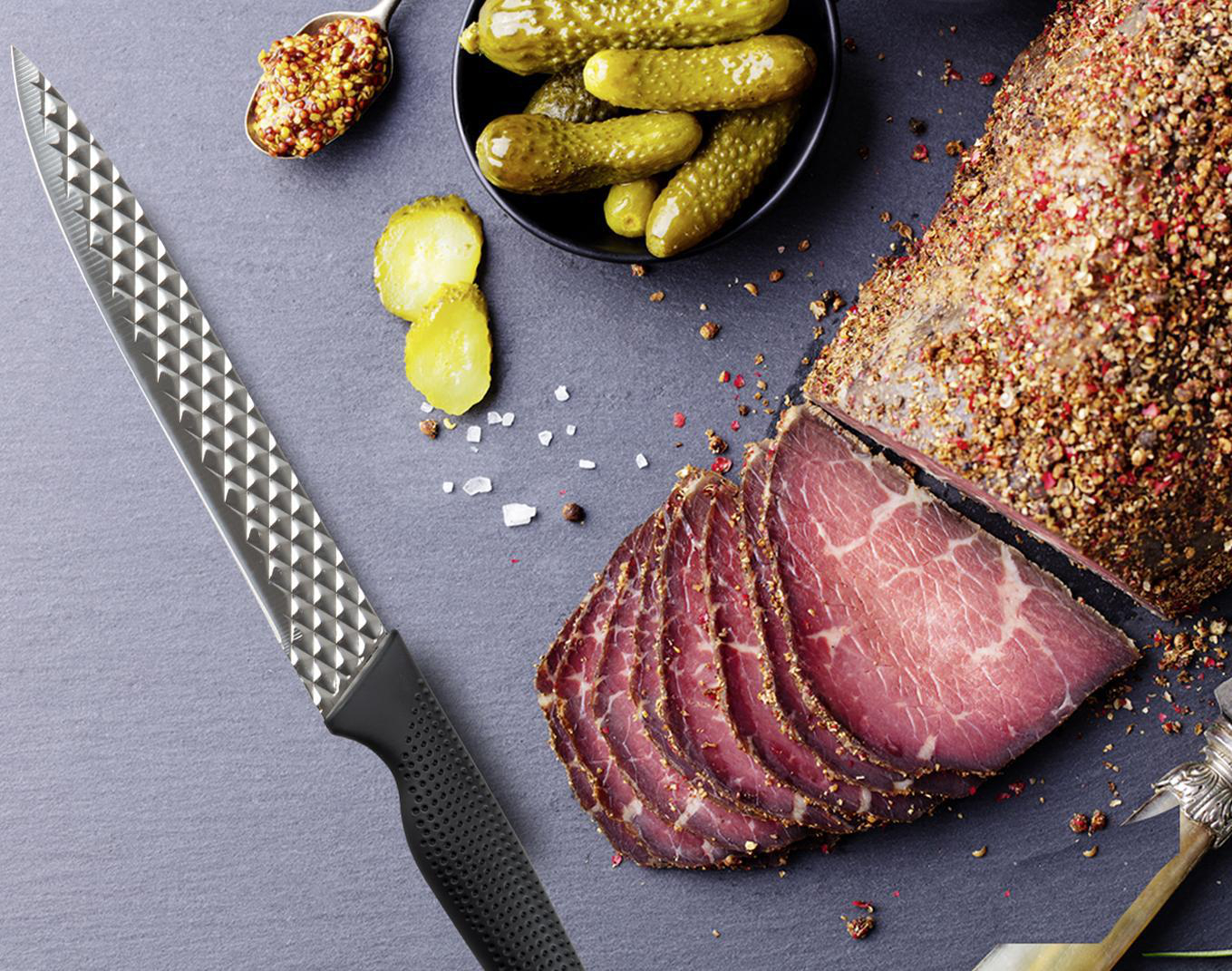 Ein Messer, geschnittenes Fleisch, Gurken und Senf auf einer dunklen Oberfläche. Messer im Vordergrund, Fleisch im Mittelgrund, Senf und Gurken im Hintergrund.