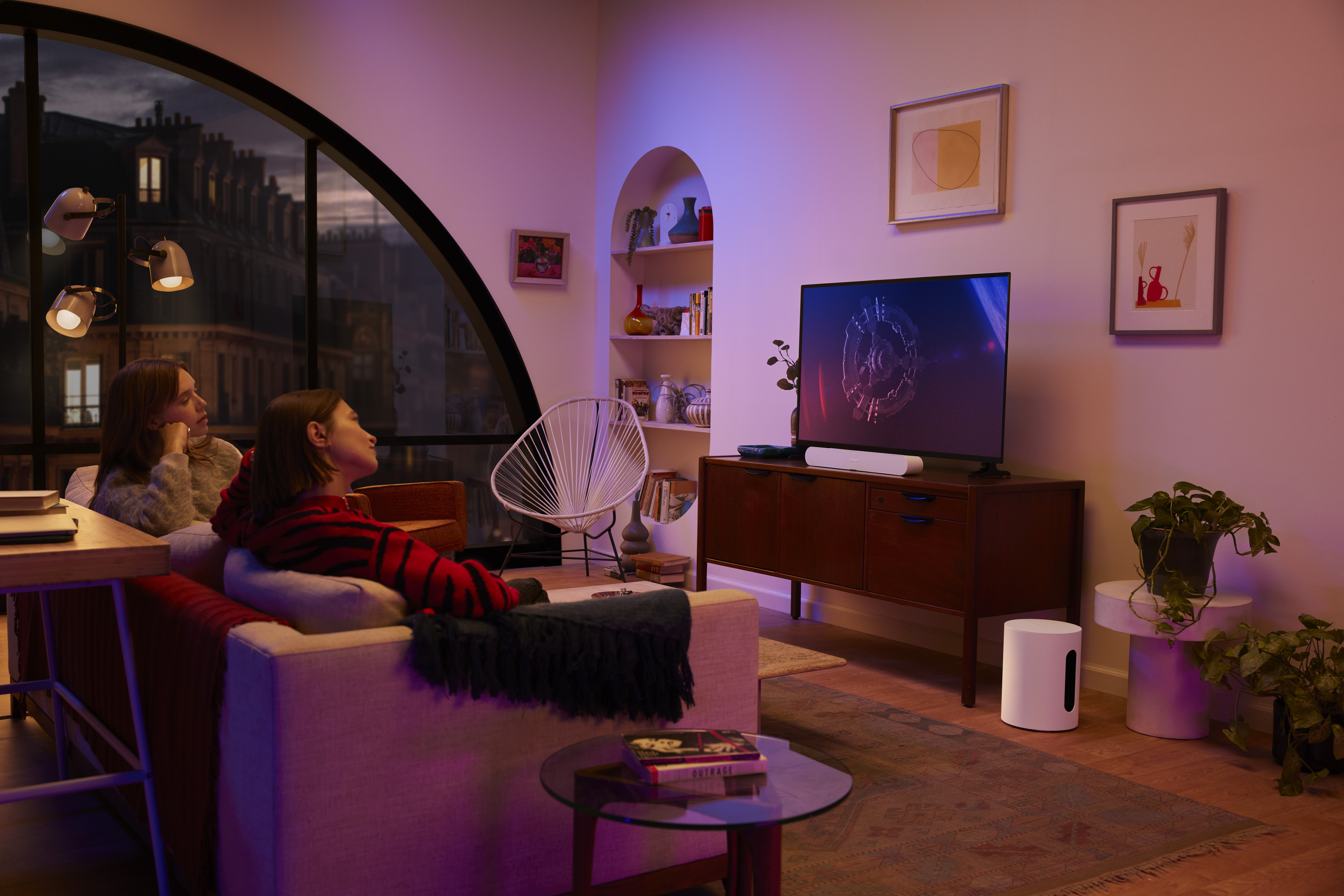 Zwei Frauen sehen fern. Weiße Soundbar, weißer Subwoofer. Gemütliches Wohnzimmer.