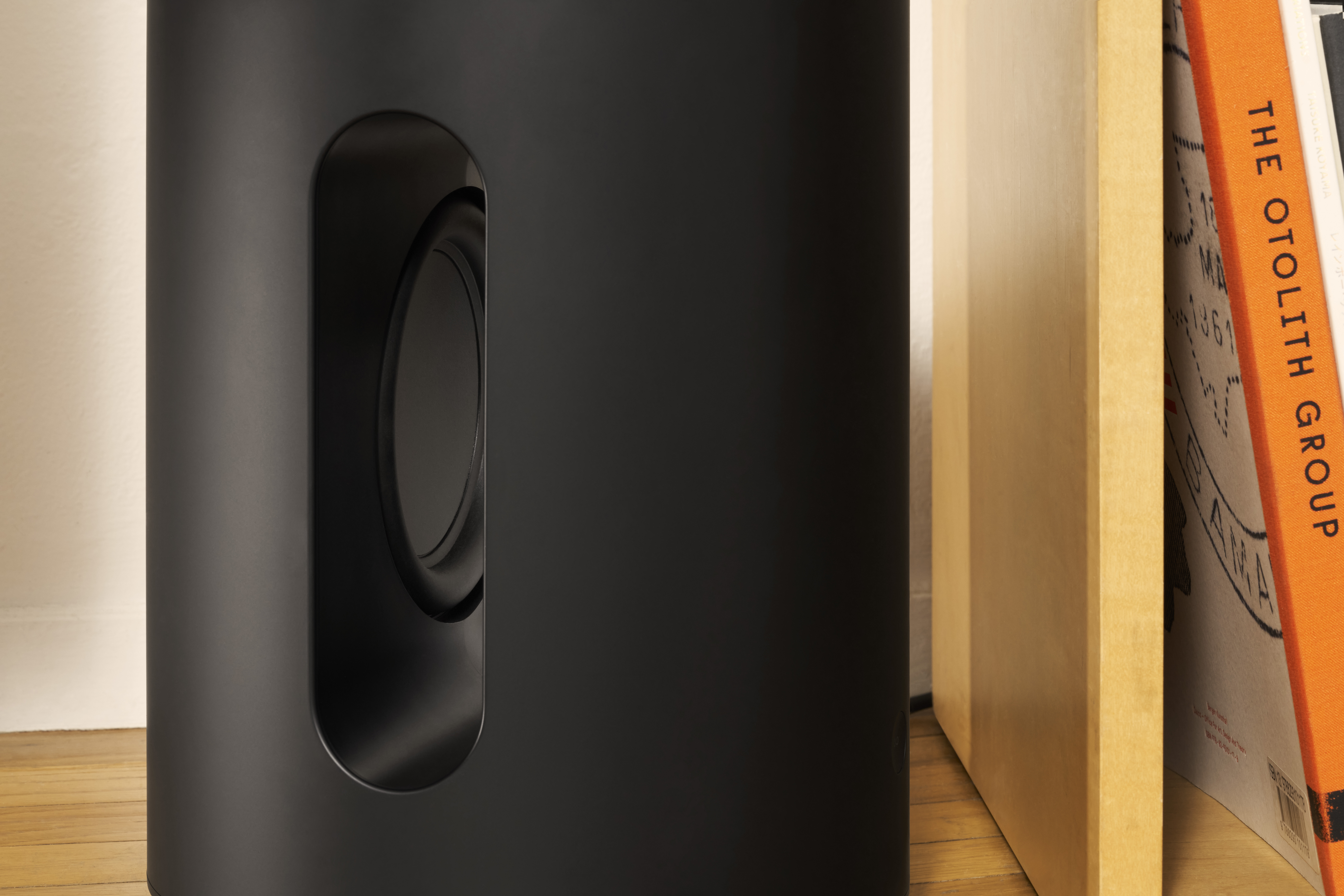 Schwarzer Subwoofer-Lautsprecher mit Seitenanschluss, neben Büchern.