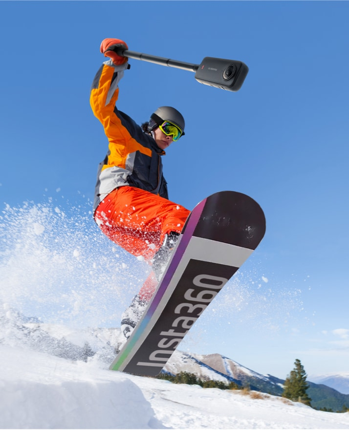 Ein Snowboarder springt in die Luft und hält eine Kamera an einer Stange.