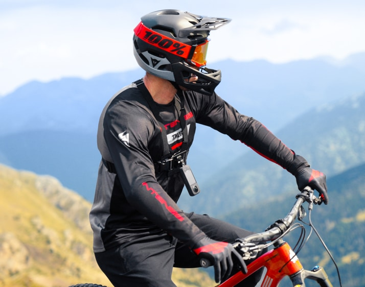 Ein Mountainbiker mit Helm mit rot-schwarzem Design. Der Fahrer ist auf einem Berg, mit Bergen im Hintergrund.