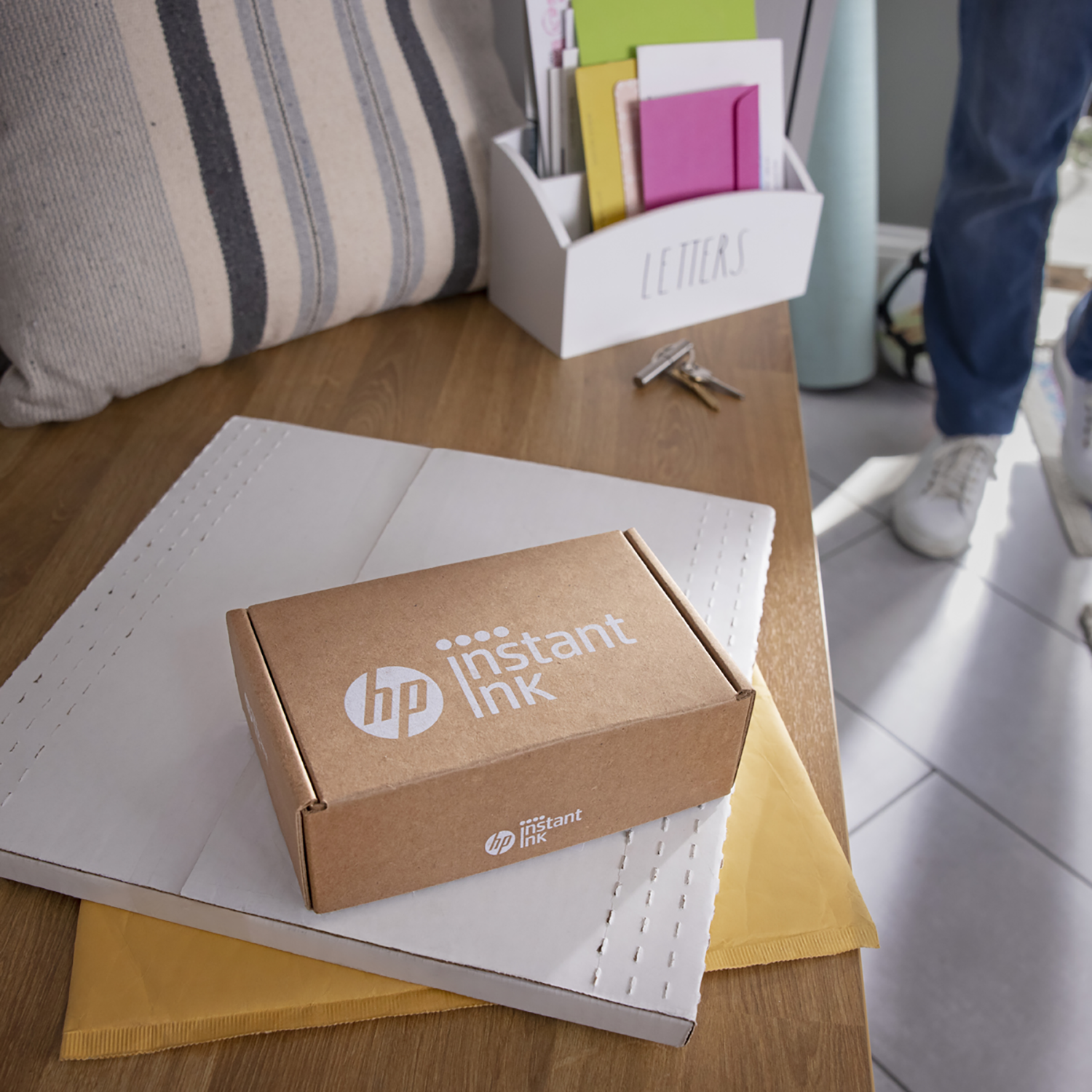 Een doos met 'HP Instant Ink' op een bureau, naast witte en gele enveloppen.