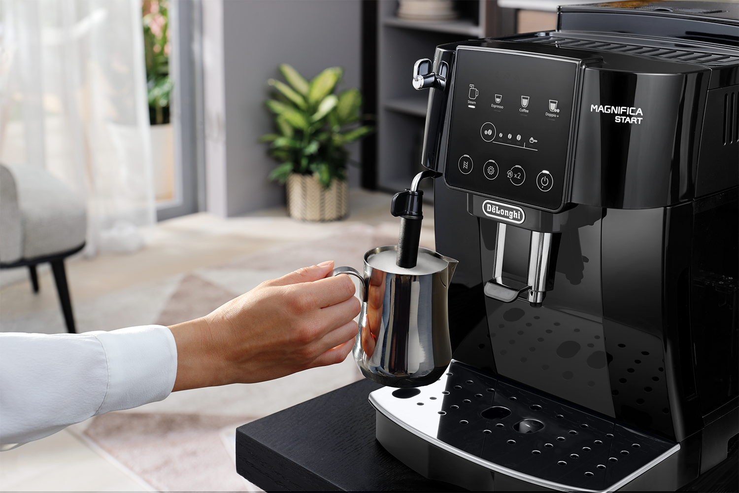 Black espresso machine with a woman's hand frothing milk with it.