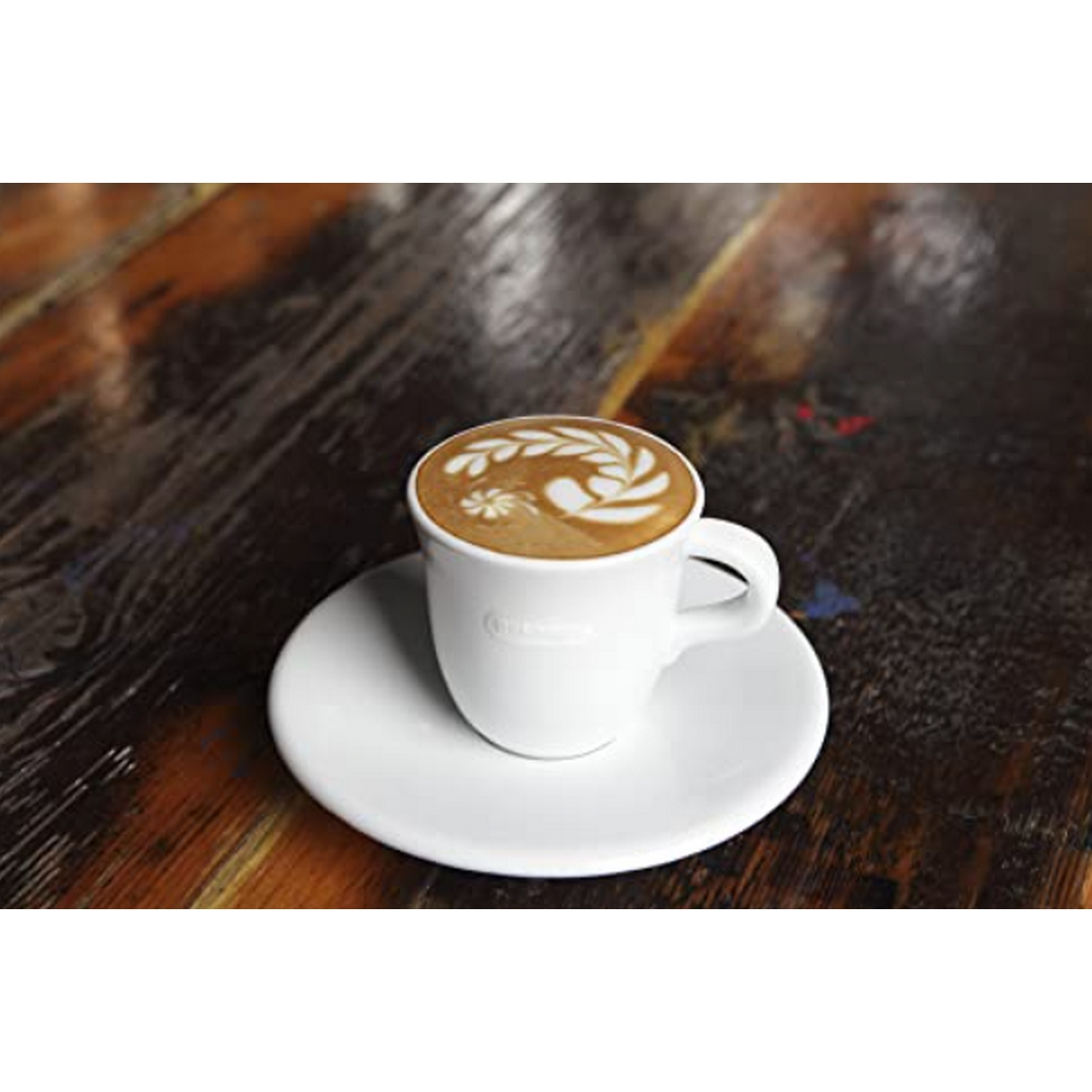 Arte latte en taza blanca sobre platillo blanco, sobre mesa de madera oscura.