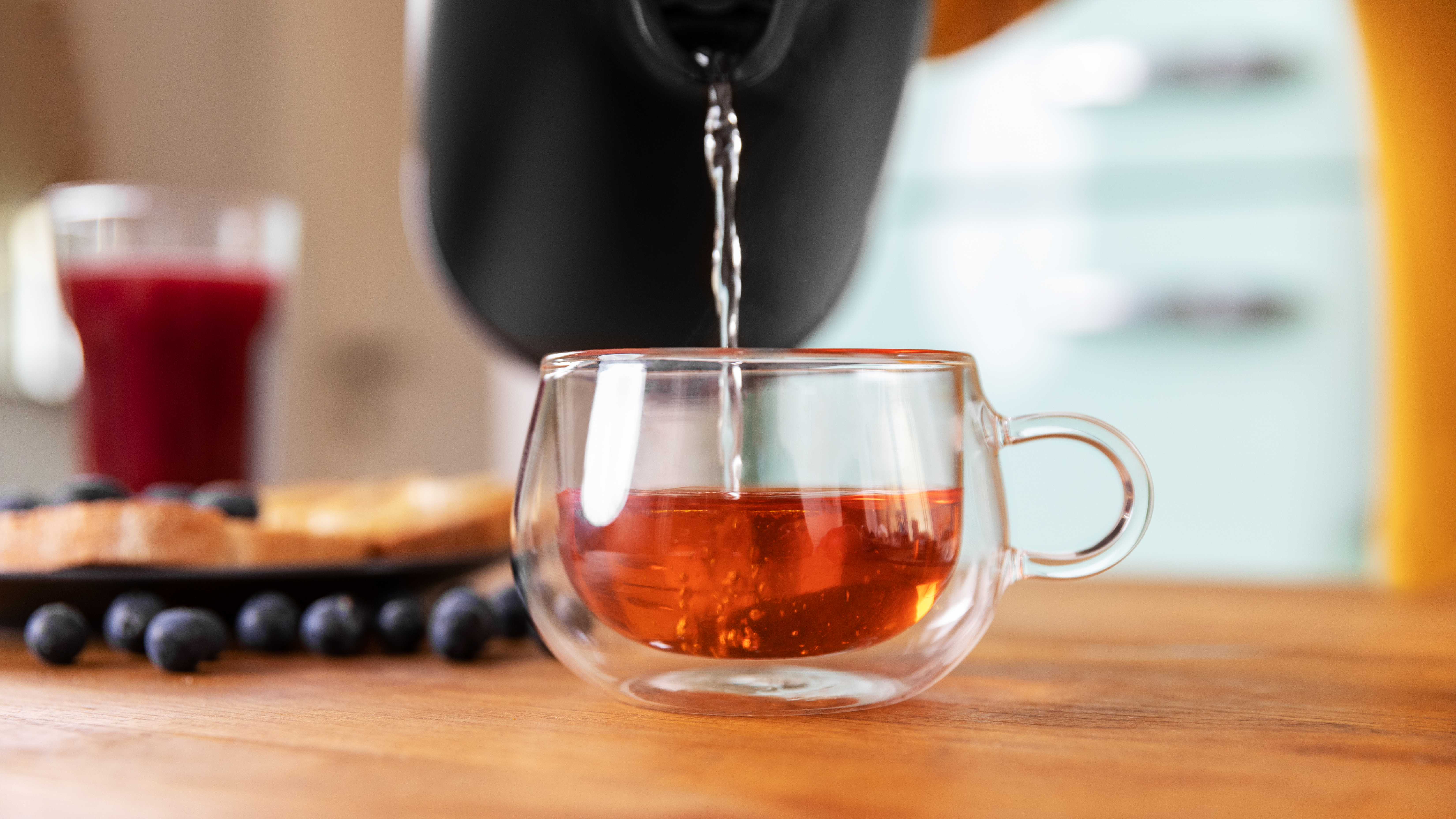 Se vierte agua en una taza de cristal transparente. Tostadas y arándanos están en el fondo.