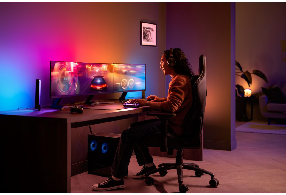 Man gaming. Three monitors show a car game. RGB lights are on the walls and desk.