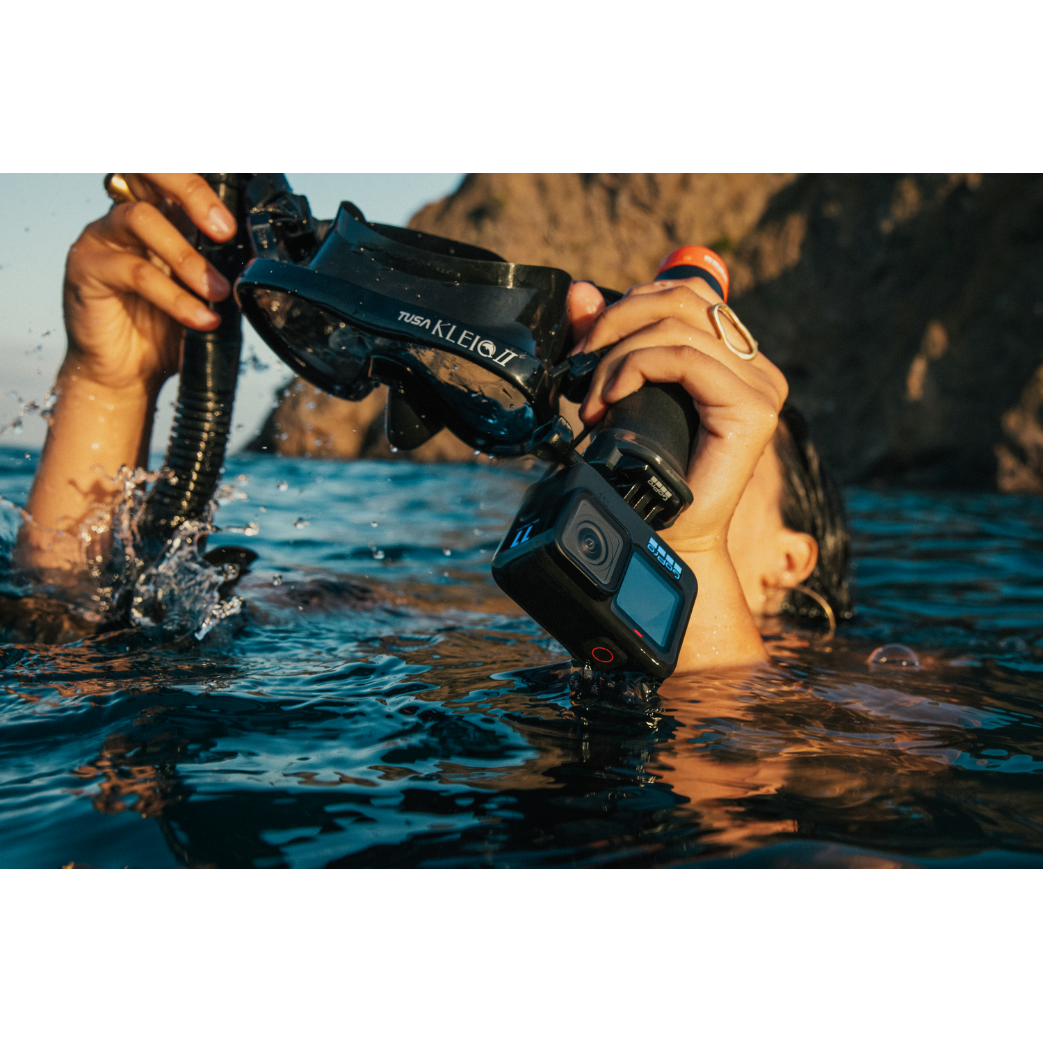 Persona en el agua sosteniendo una máscara de buceo negra y una cámara GoPro.