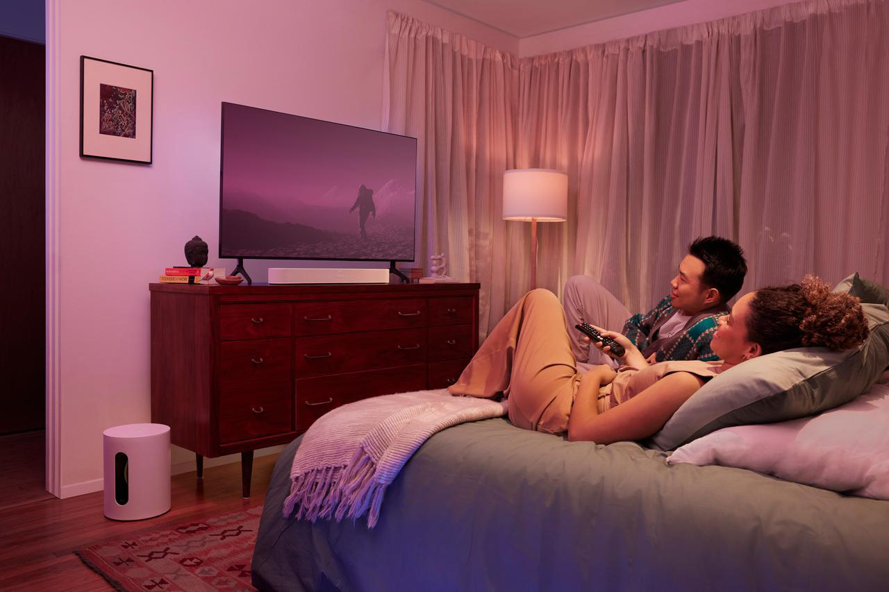 Ein Paar entspannt sich auf einem Bett und schaut fern in einem gemütlichen, beleuchteten Raum.