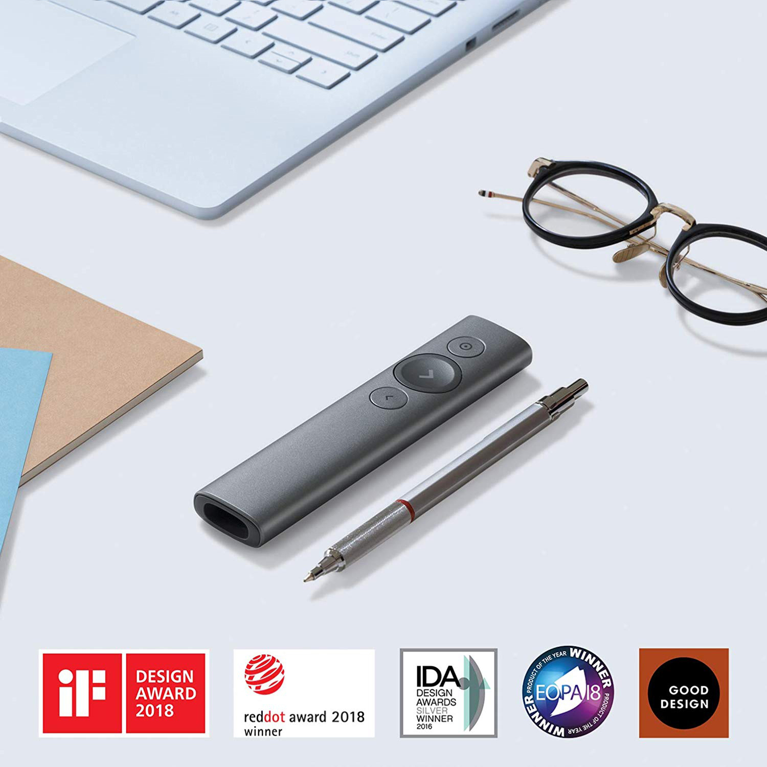 Scrivania con laptop, telecomando, penna, occhiali e premi di design.