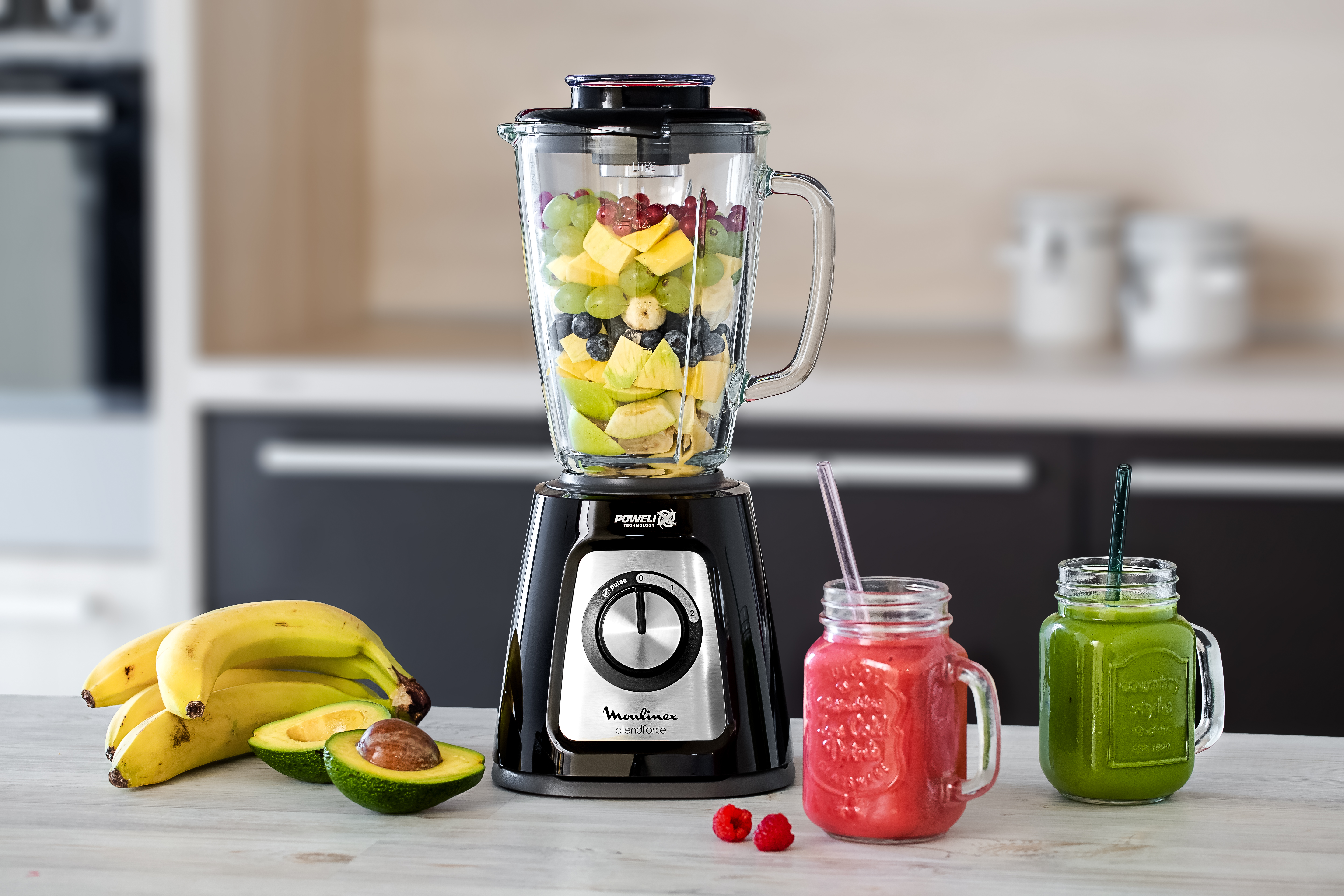 Una licuadora llena de fruta está sobre una mesa, junto con batidos e ingredientes.