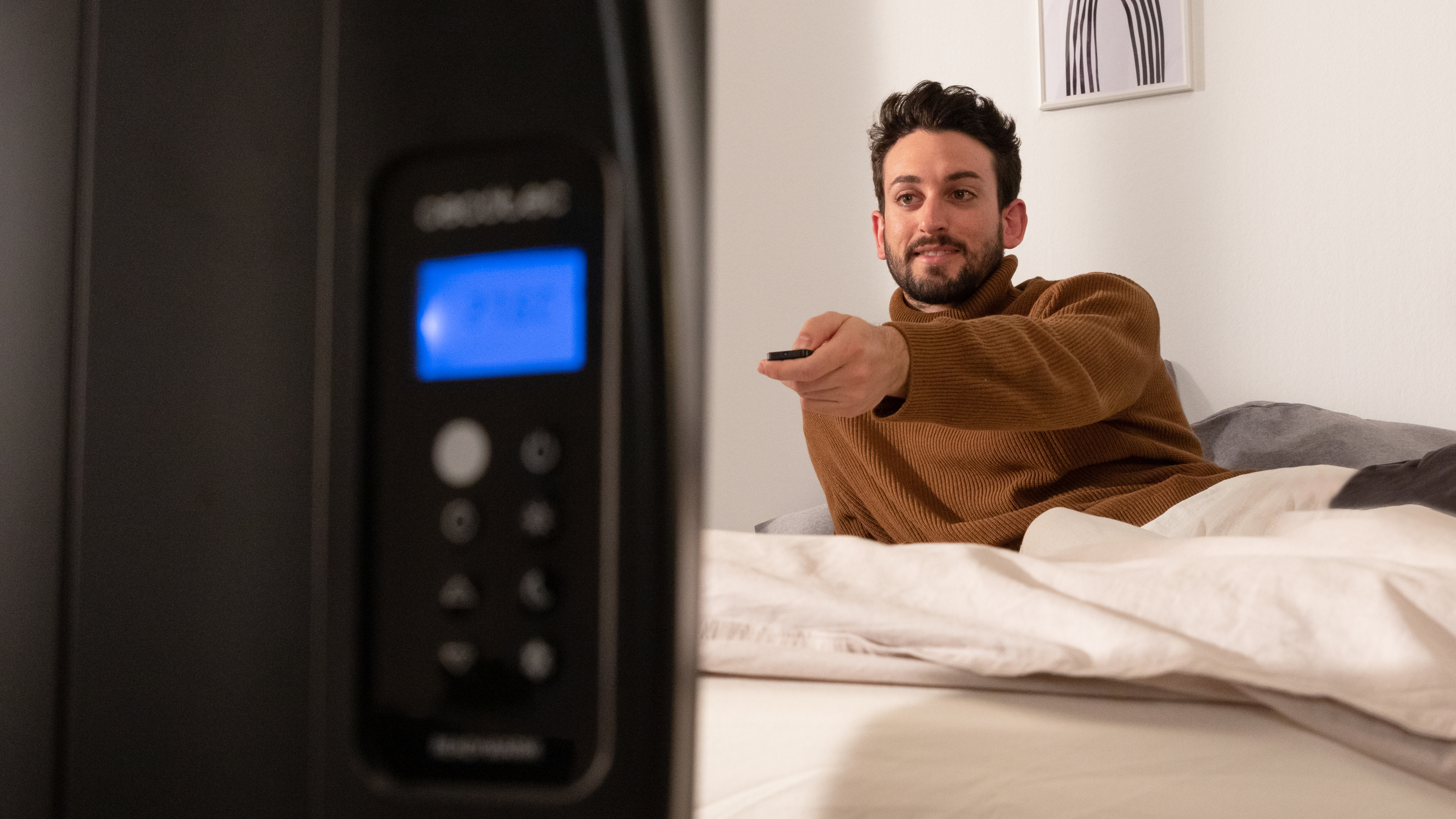 Un hombre está en la cama, sosteniendo un mando a distancia, mirando la pantalla del televisor.