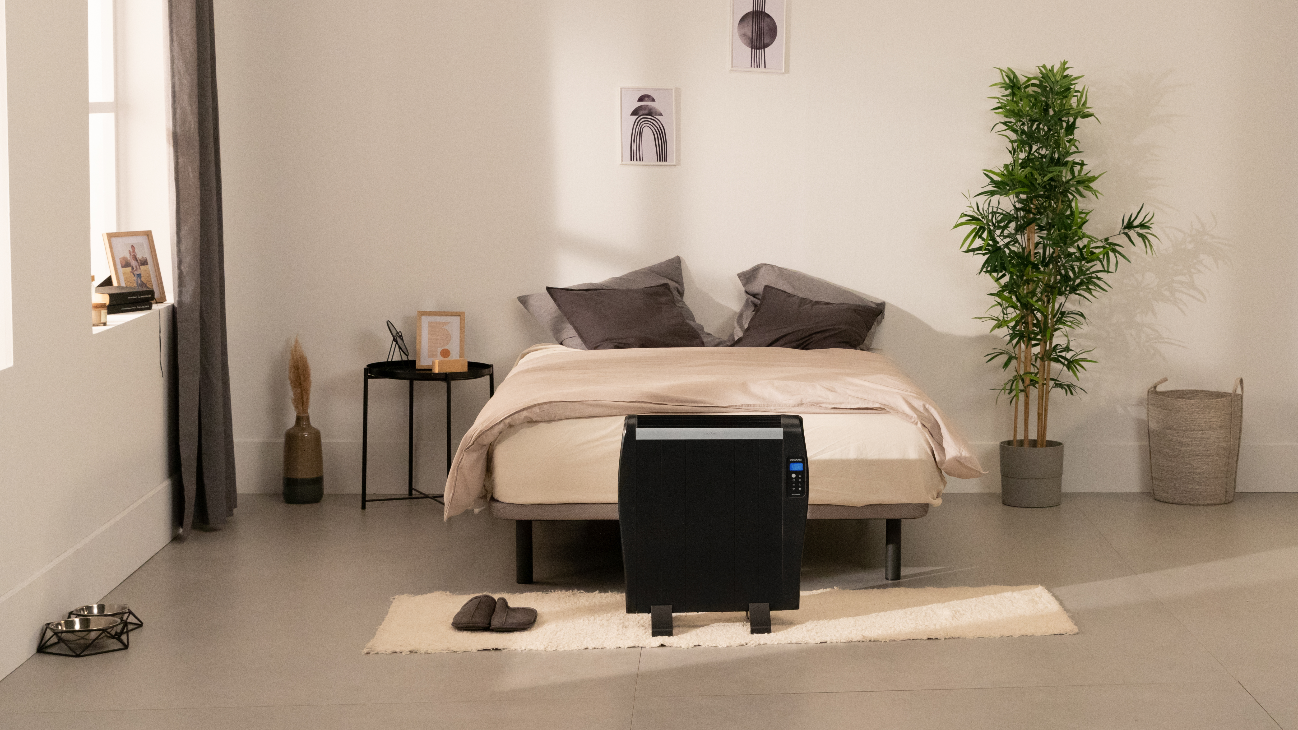 Escena de dormitorio con una cama, un calentador y una planta. La habitación tiene un esquema de color claro.