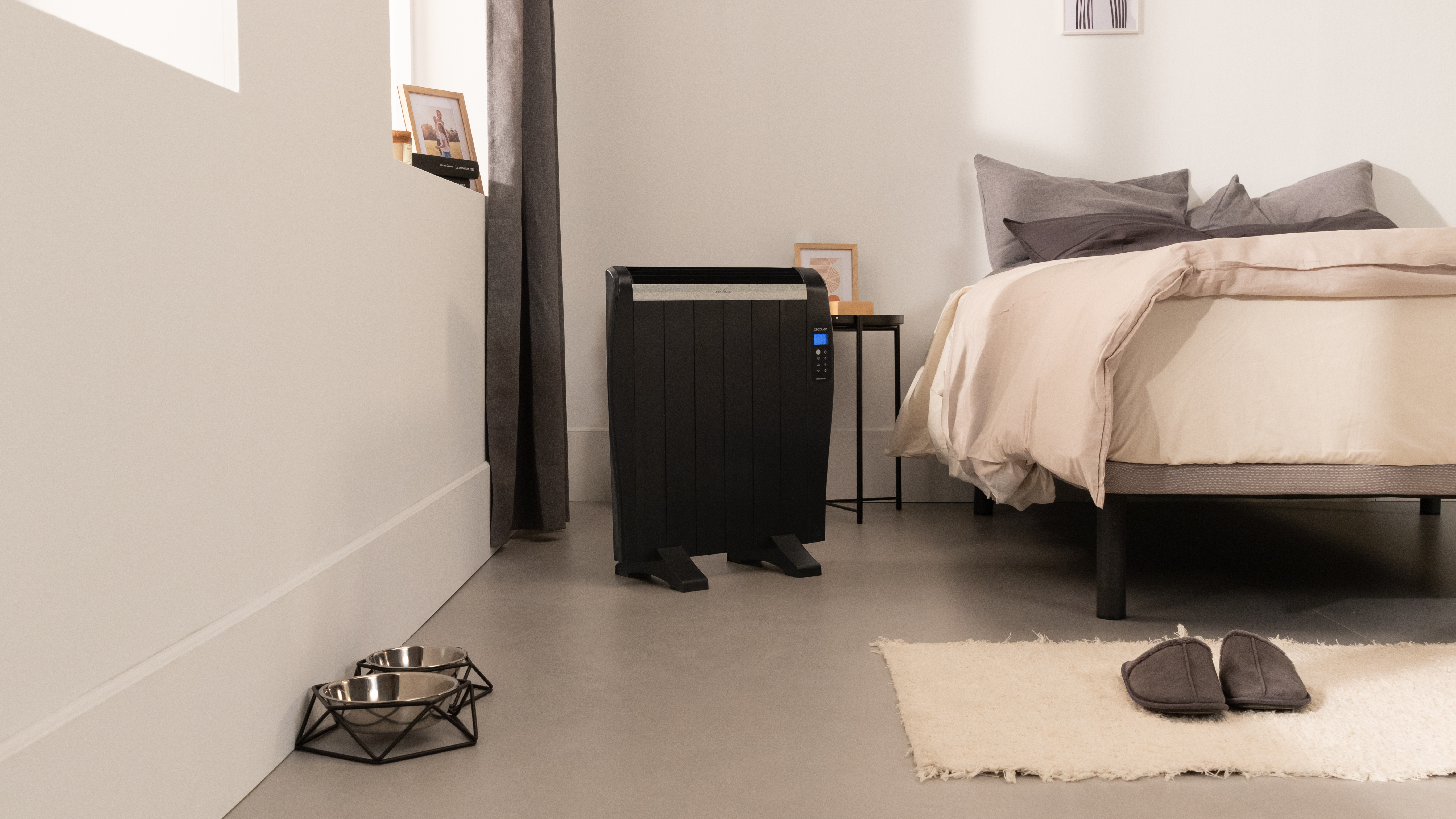 Un dormitorio con un calentador negro, cama y cuencos para mascotas.