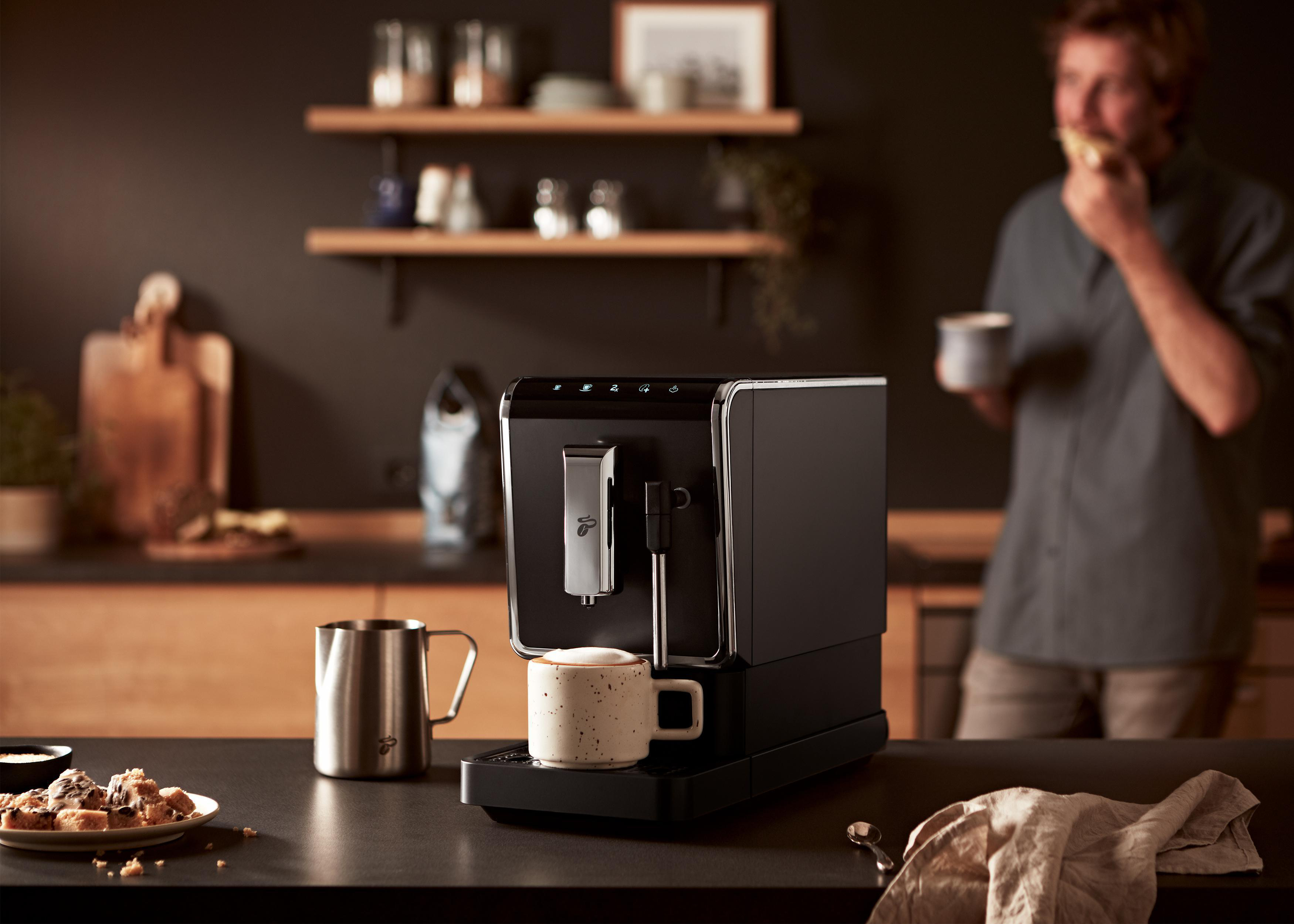 Schwarze Kaffeemaschine mit Edelstahlzubehör und ein Mann isst.