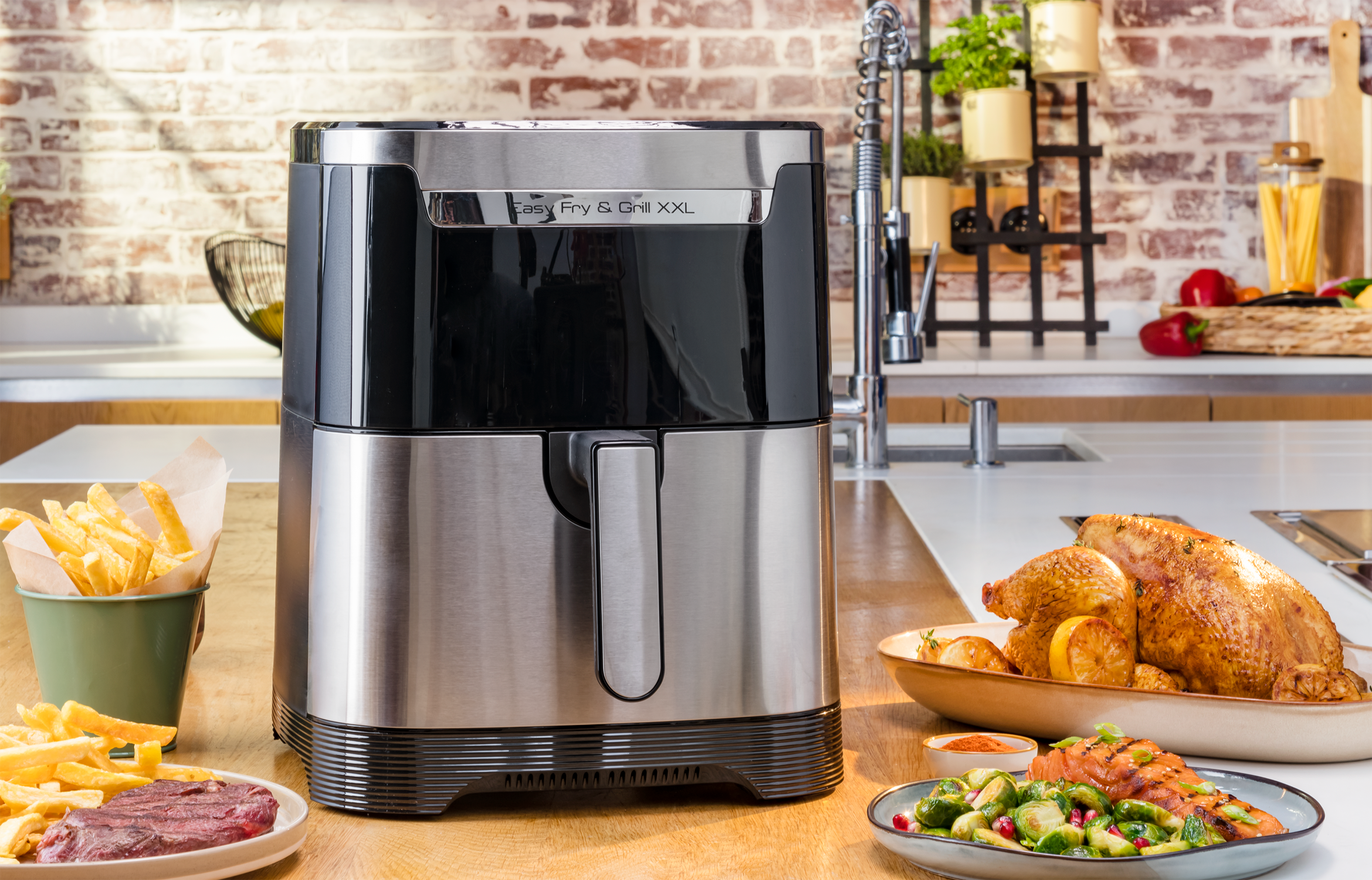 An air fryer with food including fries, steak, and a roasted chicken, on a table.