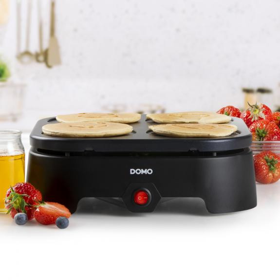 Une machine à crêpes noire avec des crêpes, des fraises et des myrtilles sur une table.