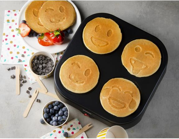 Machine à pancakes avec pancakes smiley, baies et pépites de chocolat sur une table.
