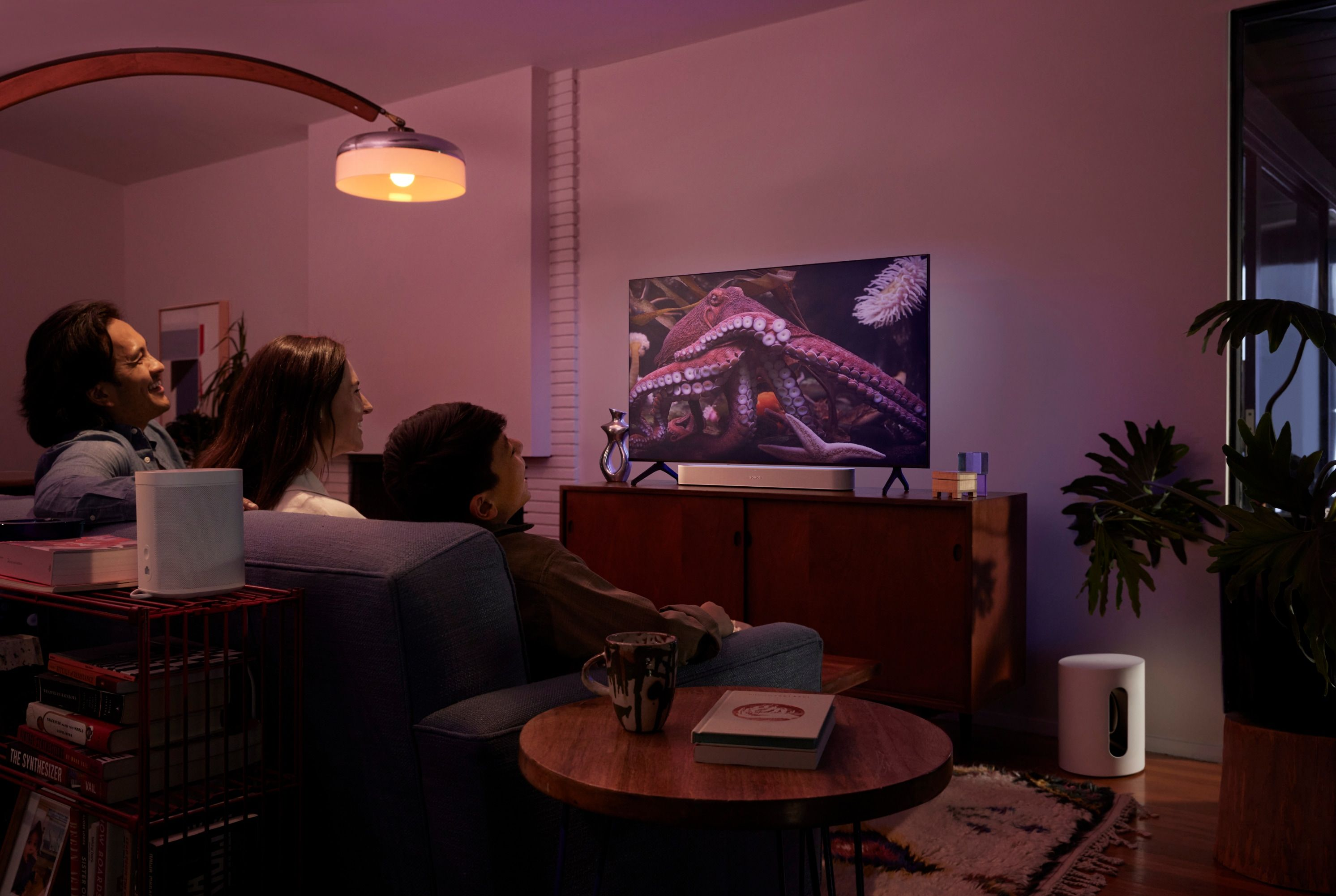 Tre persone guardano la TV che mostra un'immagine di un polpo, in una stanza con arredi e illuminazione moderni.