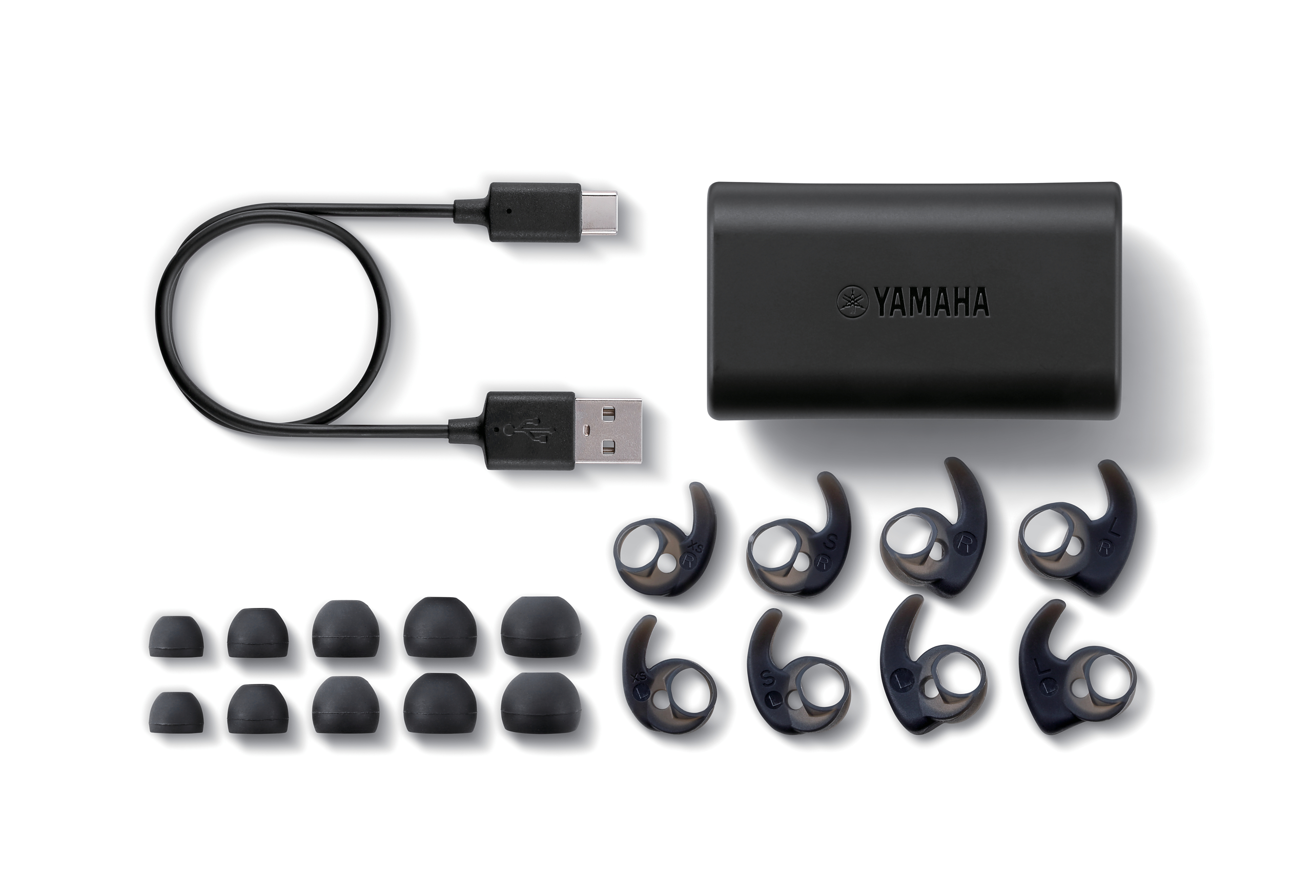 Ohrhörer, Ladeetui und Zubehör auf einer weißen Oberfläche. Ein USB-Kabel ist ebenfalls vorhanden.