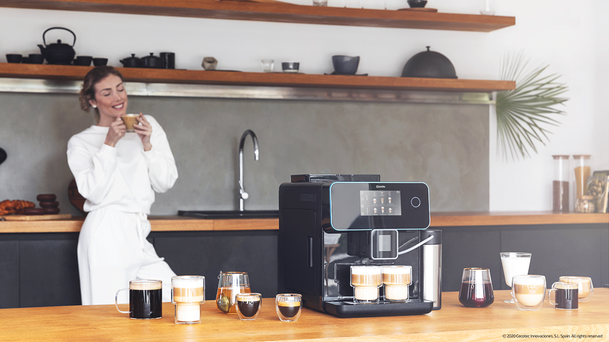 Una mujer con una taza de café cerca de una cafetera y tazas.