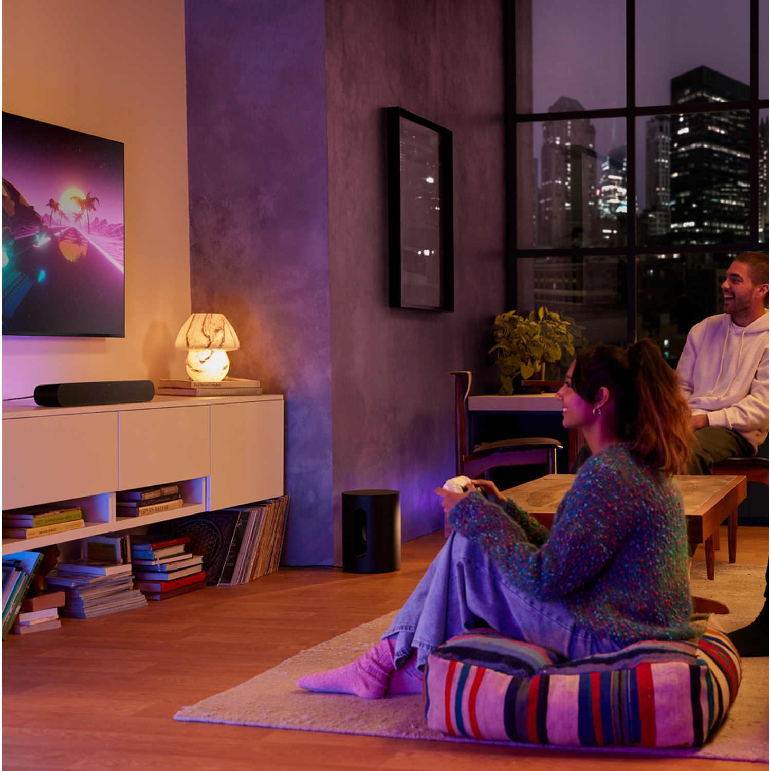 Escena con personas, TV, subwoofer y una alfombra. Una mujer sonríe.