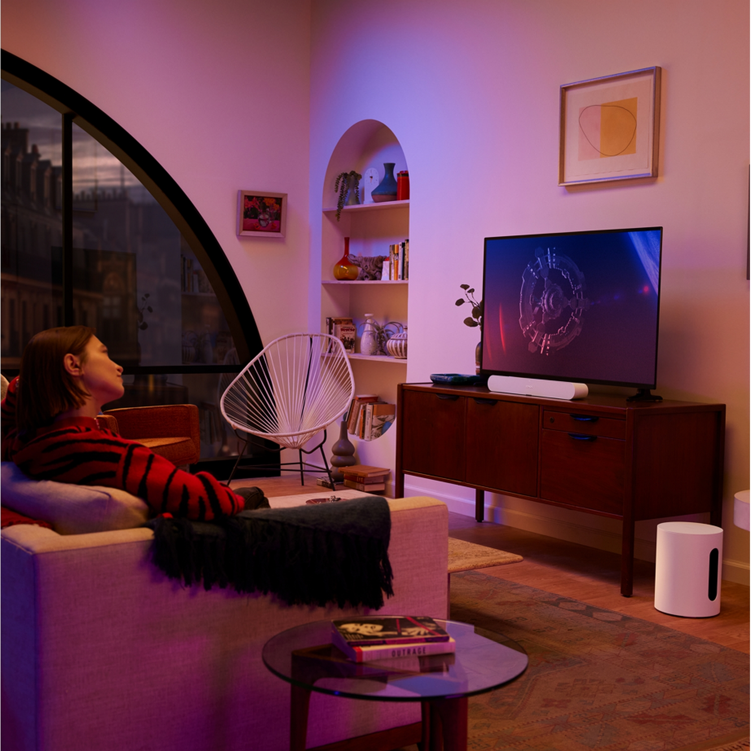 Una mujer mira la televisión en una sala de estar moderna, con una barra de sonido y un subwoofer.