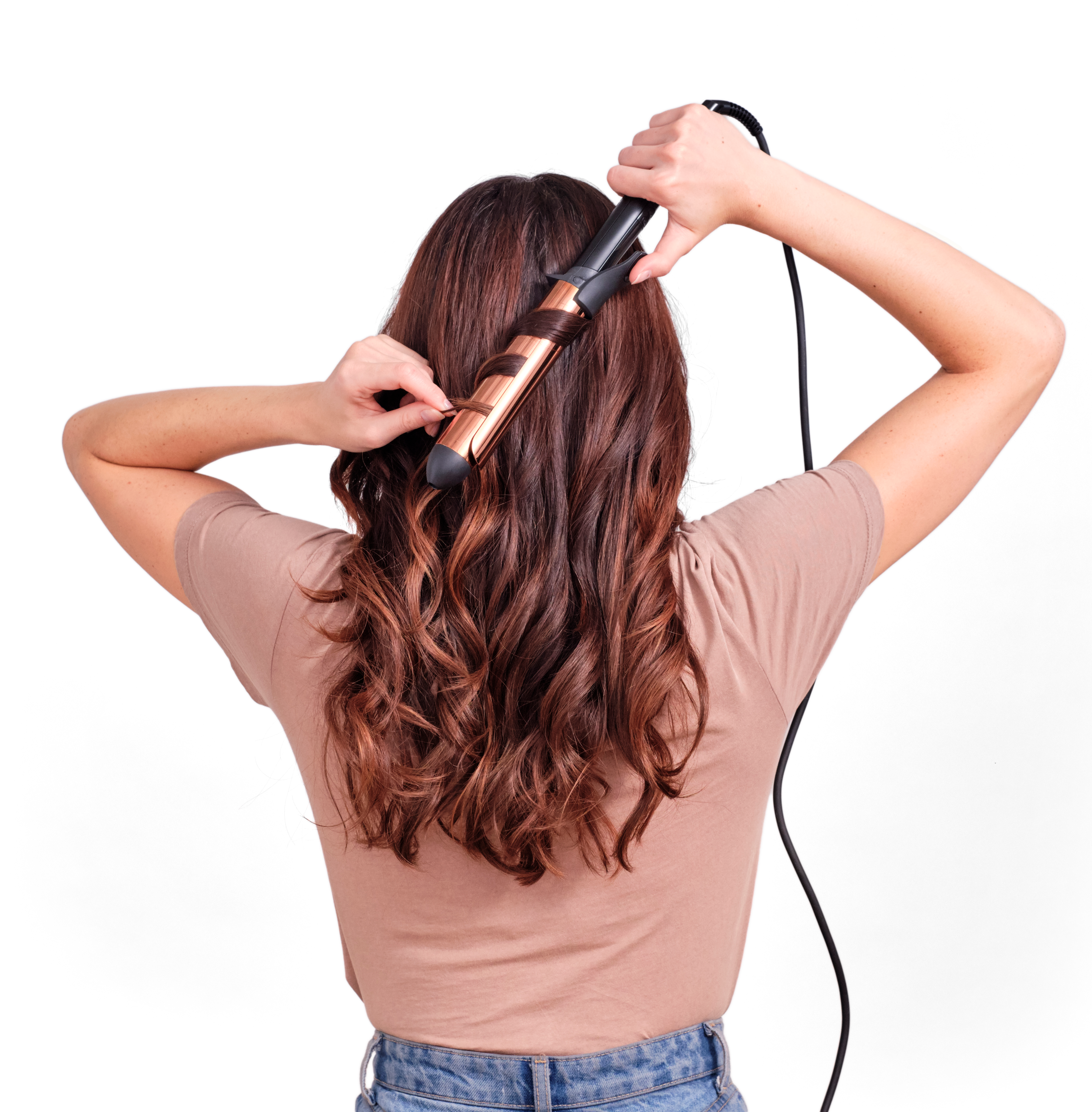 Donna che si arriccia i capelli con un ferro arricciacapelli. Vista posteriore, capelli castani, top beige, jeans blu.