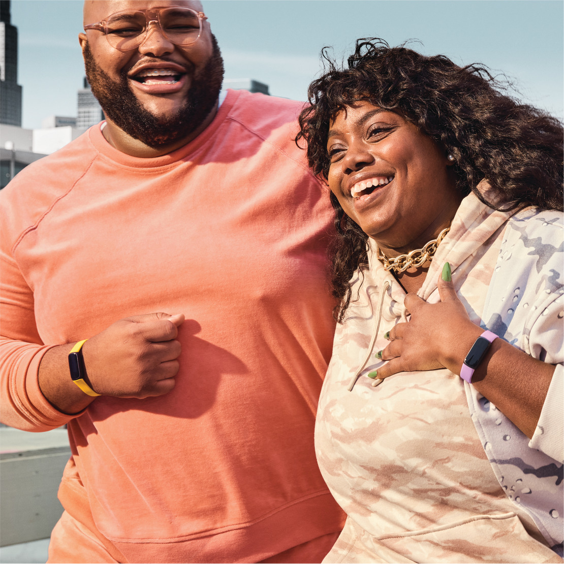 Two people smiling and laughing, wearing fitness trackers. One is yellow, one is purple.