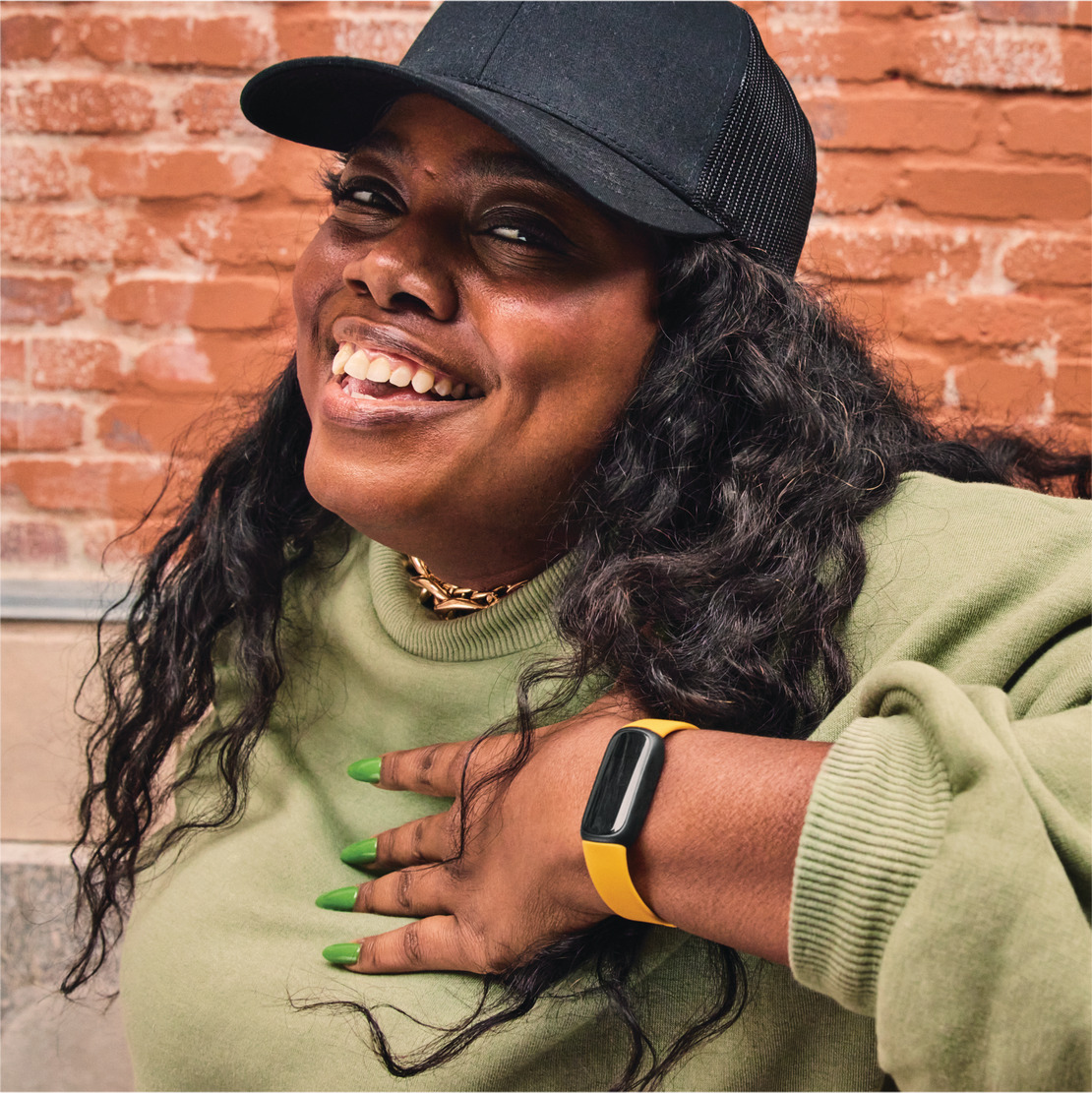 Happy woman wearing a black cap and a green top with a yellow fitness tracker.