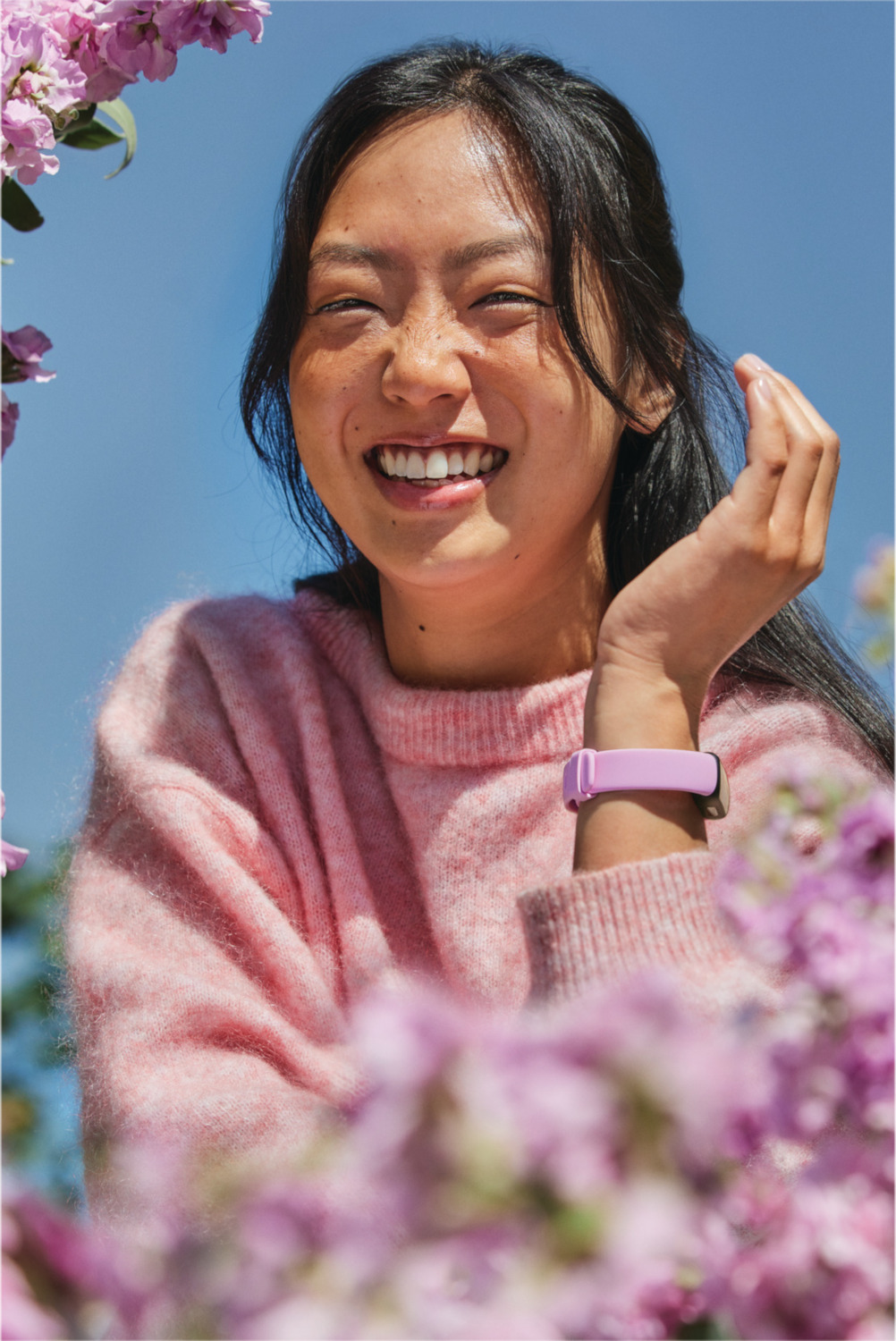 Woman smiling, wearing pink sweater, with a wristband.