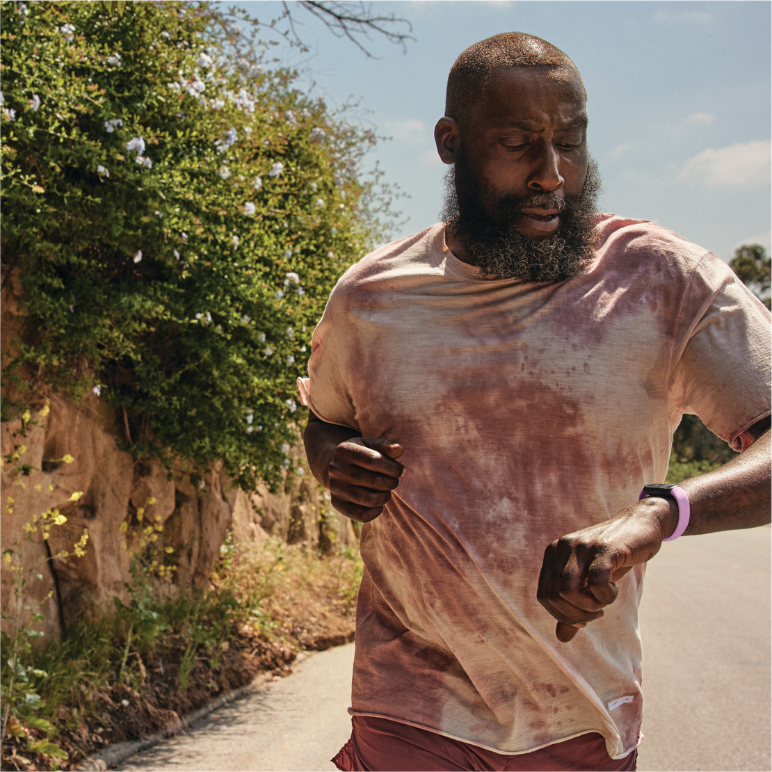 Man running outdoors, wearing a watch. He is running on a pathway next to a wall with plants.