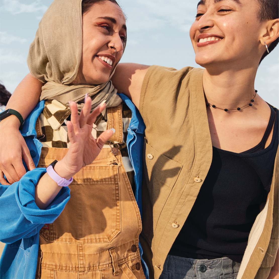 Two women smiling, one wearing a hijab and the other a necklace. They are embracing.