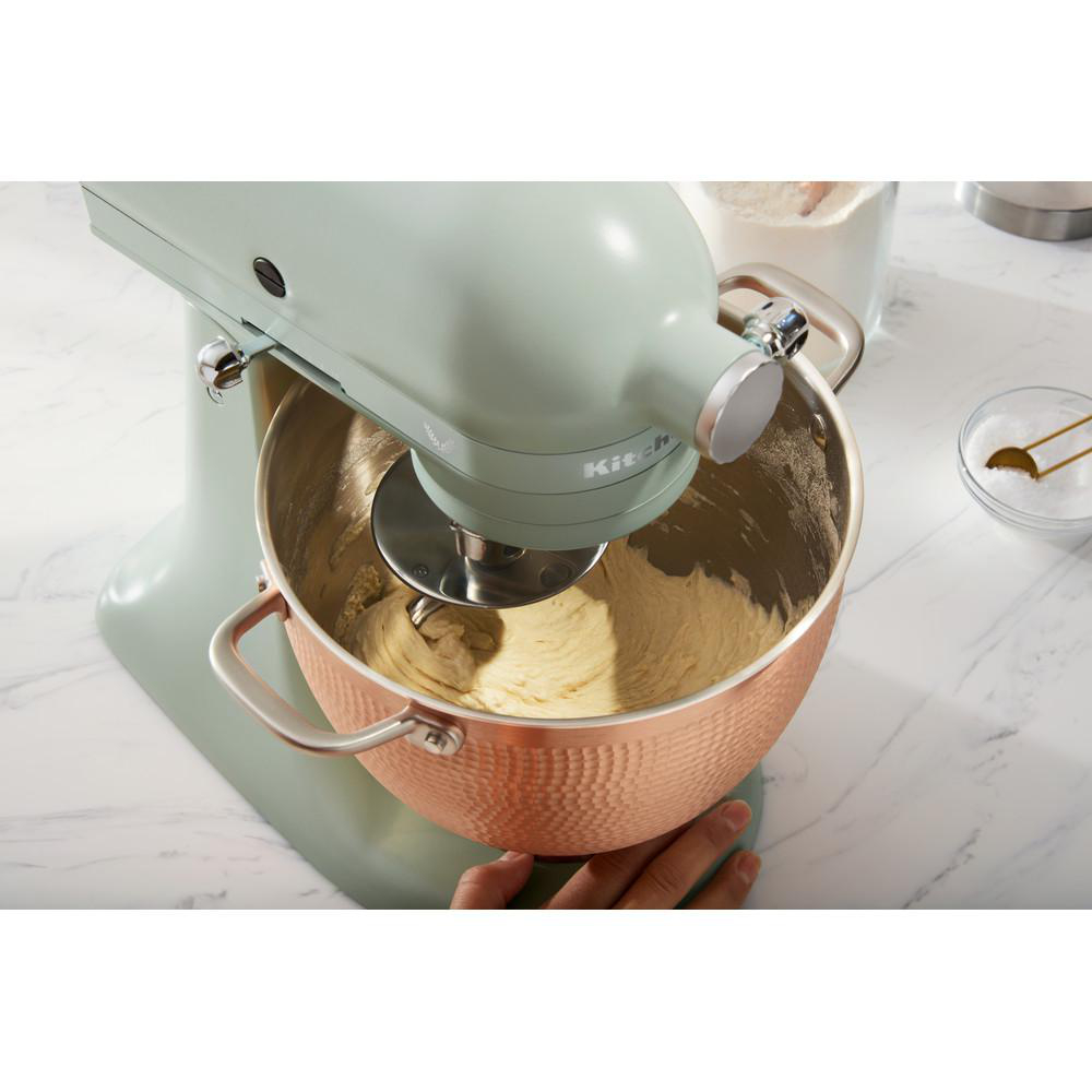 Minzfarbener Standmixer mit einer Kupfer-Schüssel, die Teig mischt. Mehl und weitere Zutaten sind sichtbar.