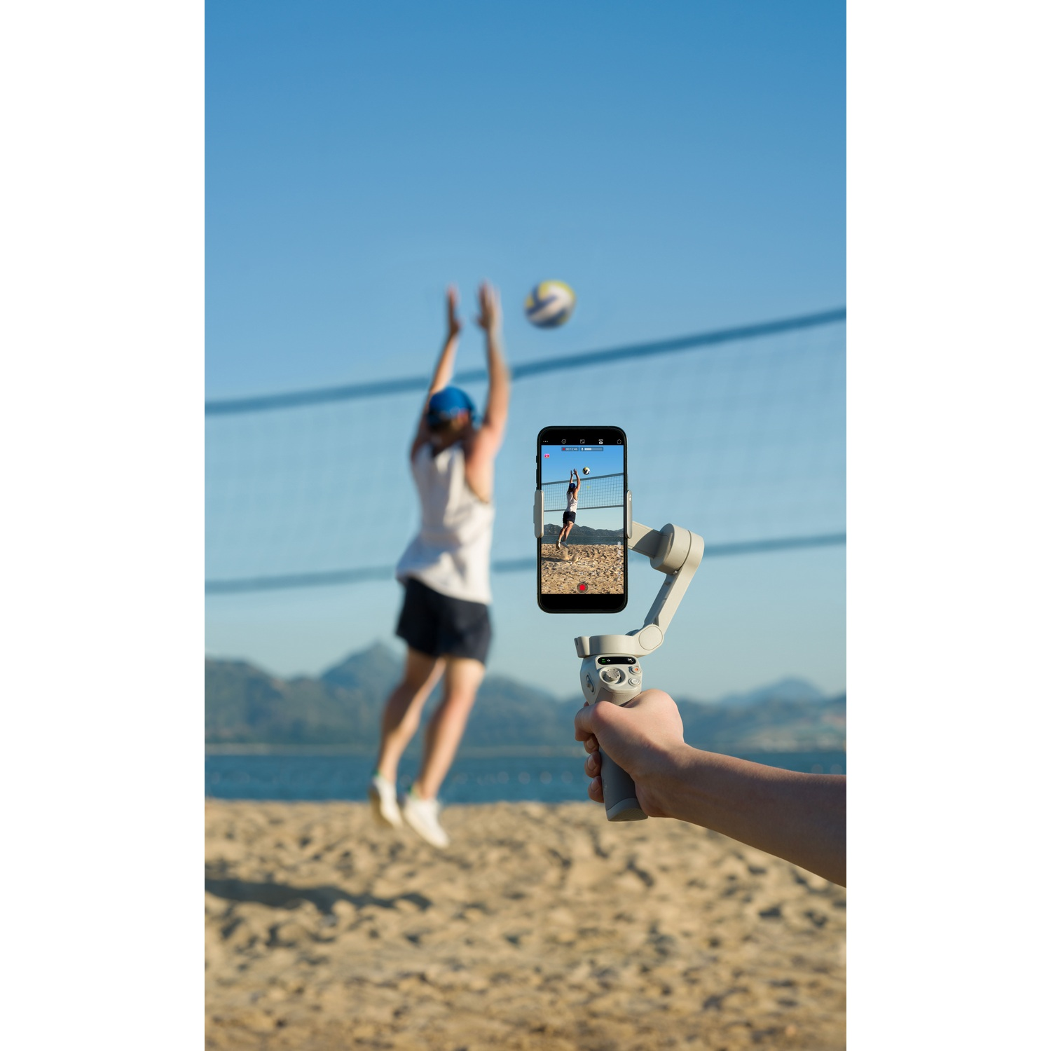 Persona grabando un partido de voleibol en la playa con un teléfono.