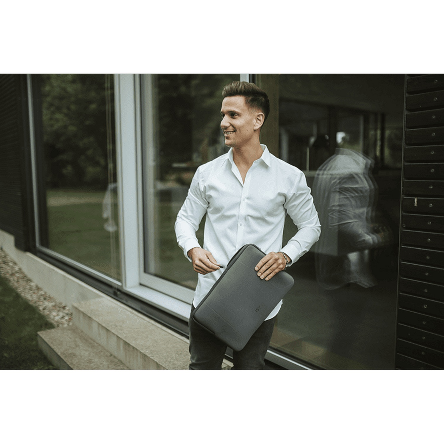 Un hombre con camisa blanca sosteniendo una funda para portátil.
