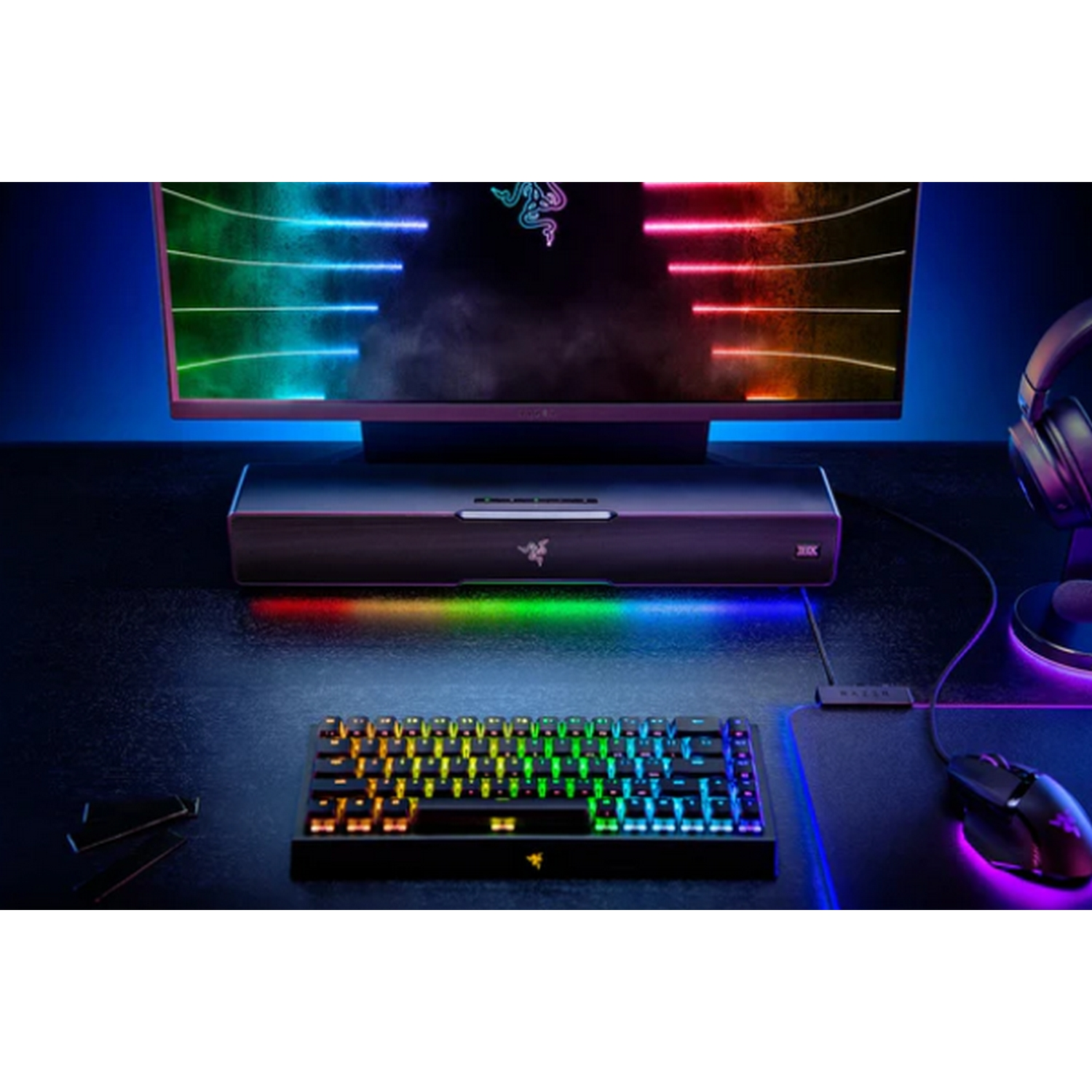 Configuración de juego con teclado, monitor, ratón y barra de sonido. Escritorio negro, luces azules y arcoíris.