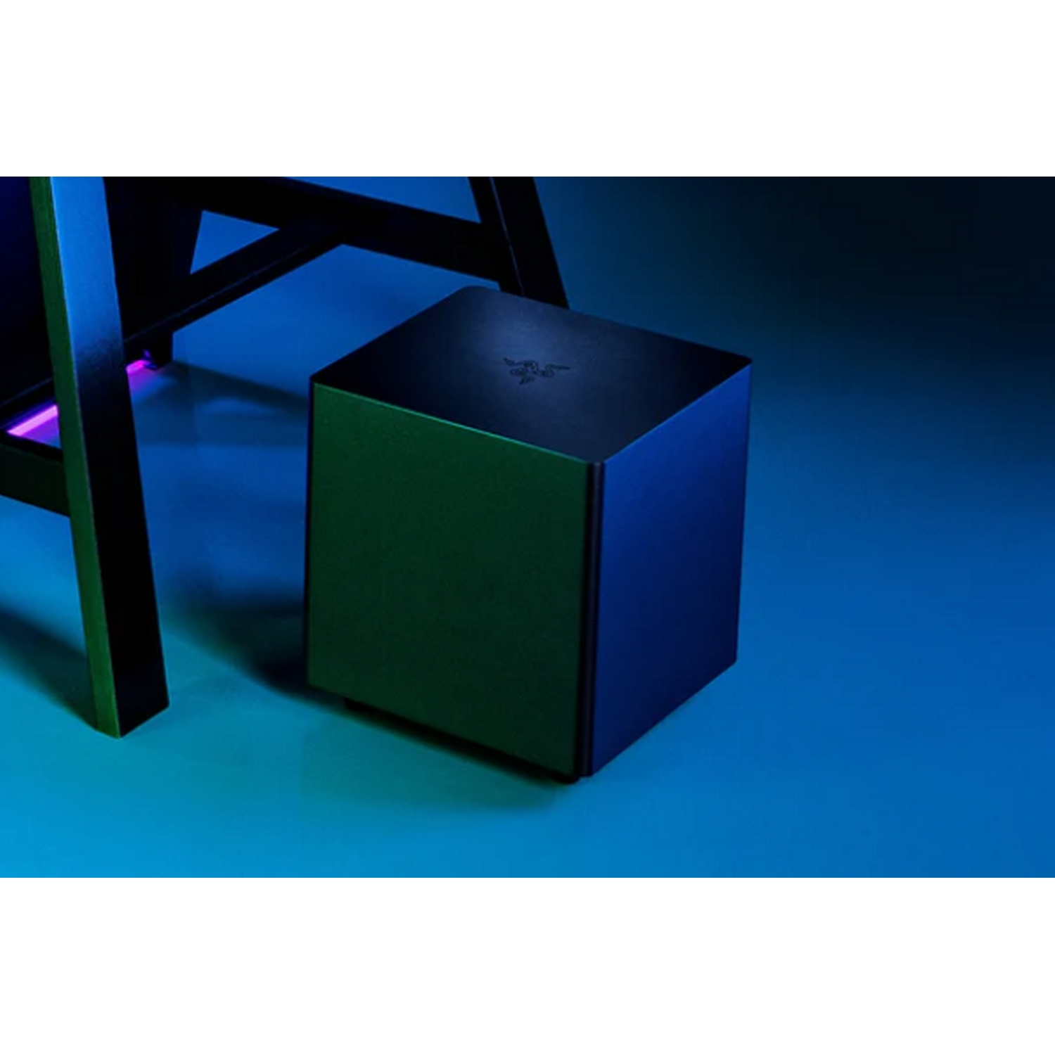 Un subwoofer Razer negro en forma de cubo sobre una superficie azul verdosa, cerca de una pata de escritorio negra.