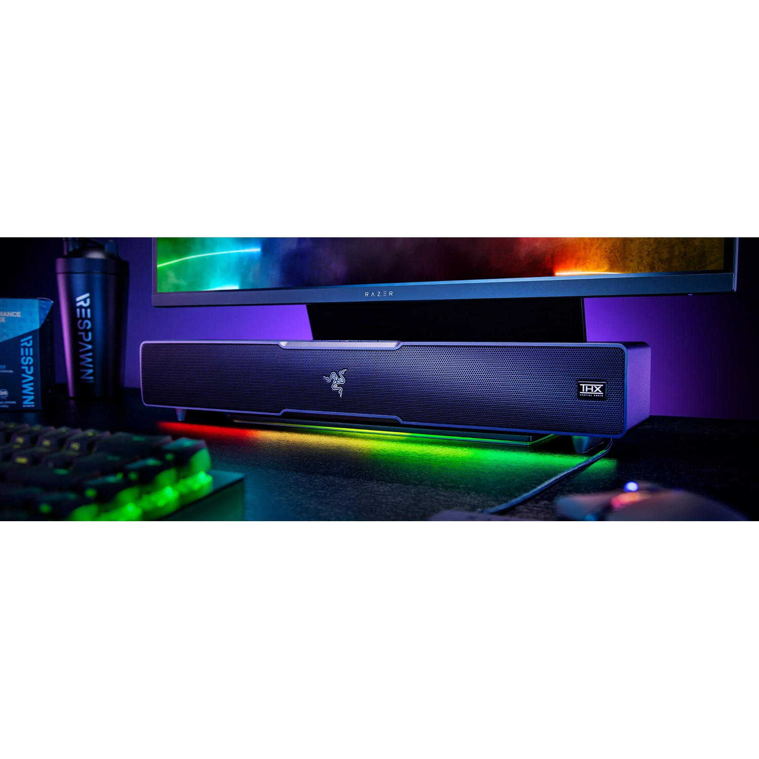 Una barra de sonido Razer está debajo de un monitor. La barra de sonido tiene el logotipo de Razer y una luz.