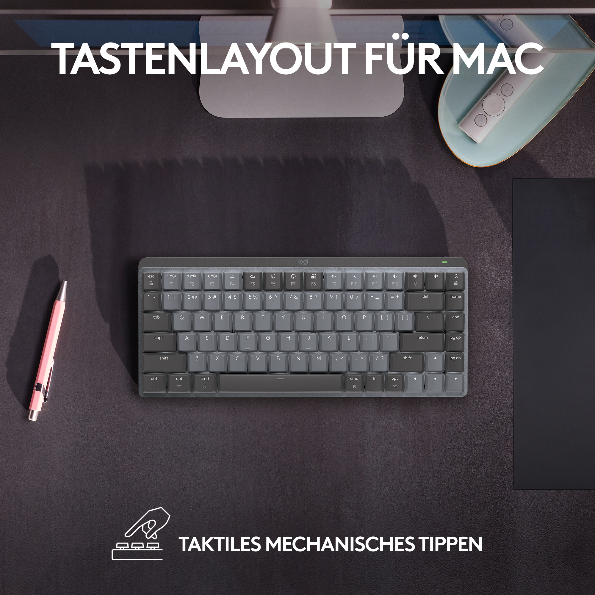 Eine Tastatur mit grauen Tasten auf dunkler Oberfläche, mit einem rosa Stift und einem Monitor.