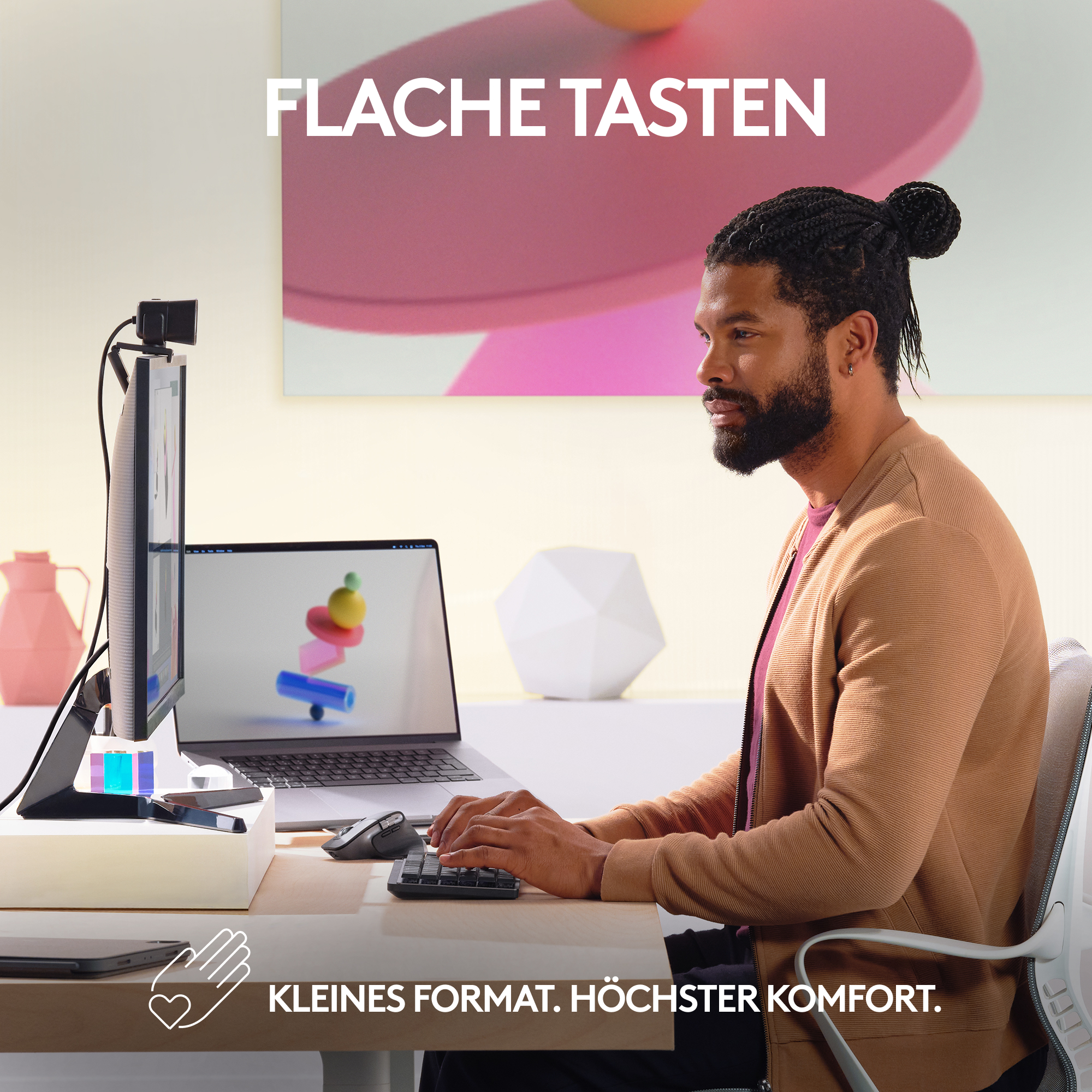 Ein Mann sitzt an einem Schreibtisch und tippt auf einer Tastatur. Ein Monitor und ein Laptop stehen vor ihm.